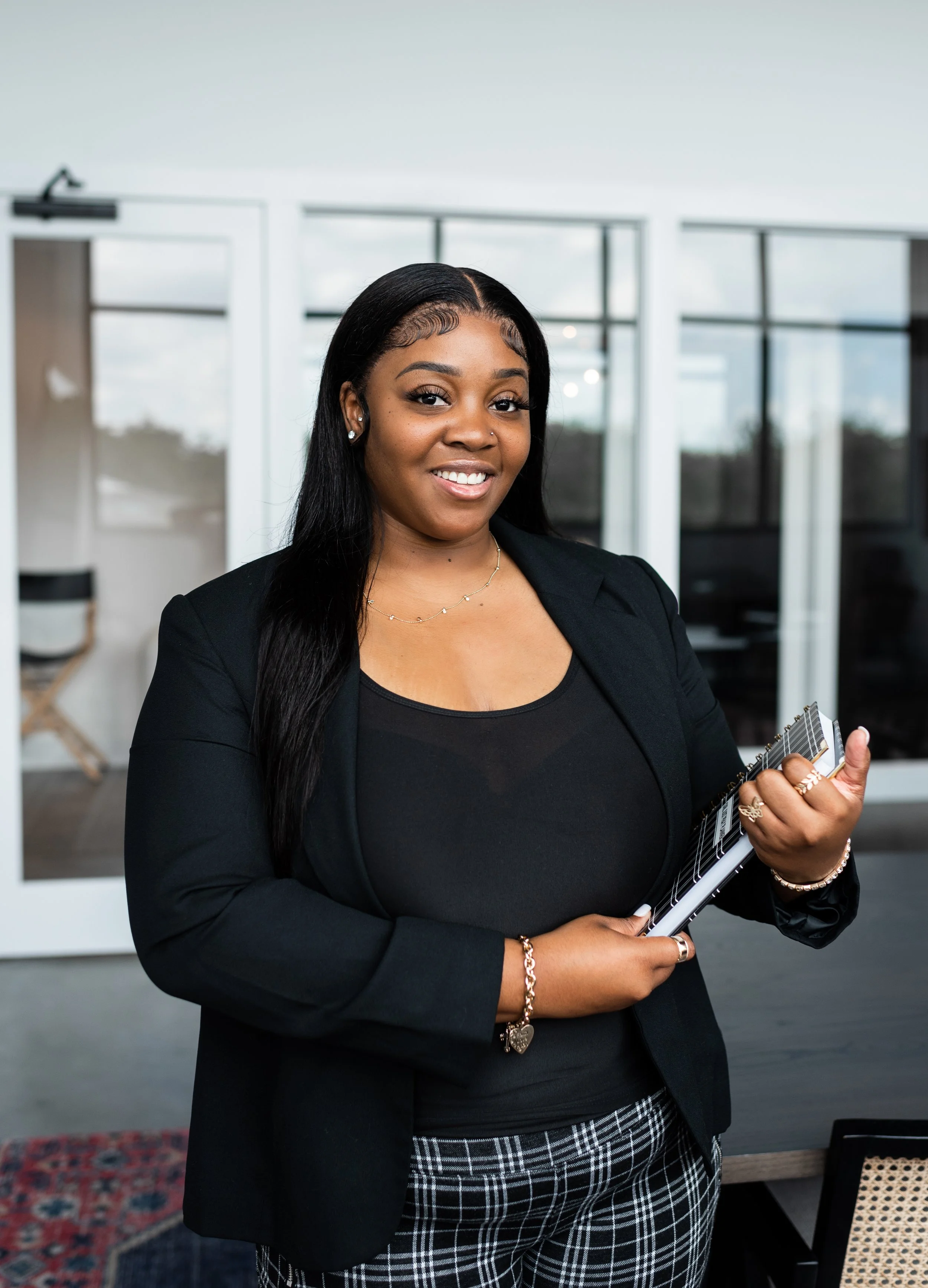 A professional woman smiling and holding a clipboard in a modern office setting.