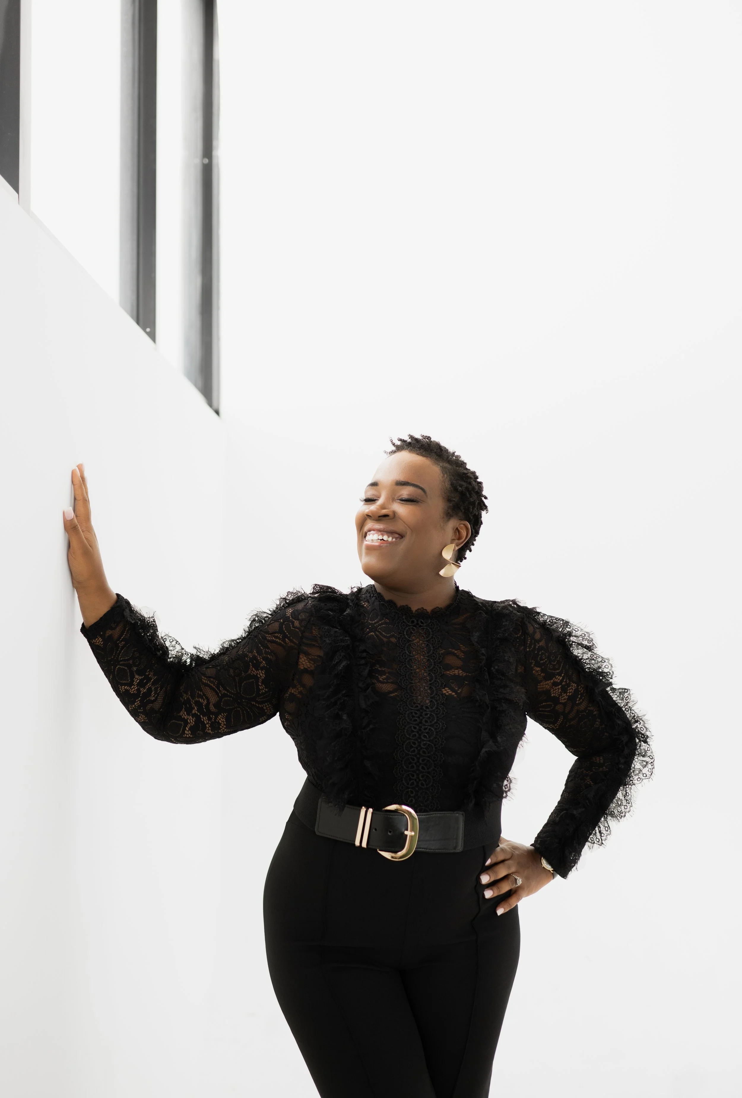 A woman smiling and leaning on a white wall in a modern, minimalist space.