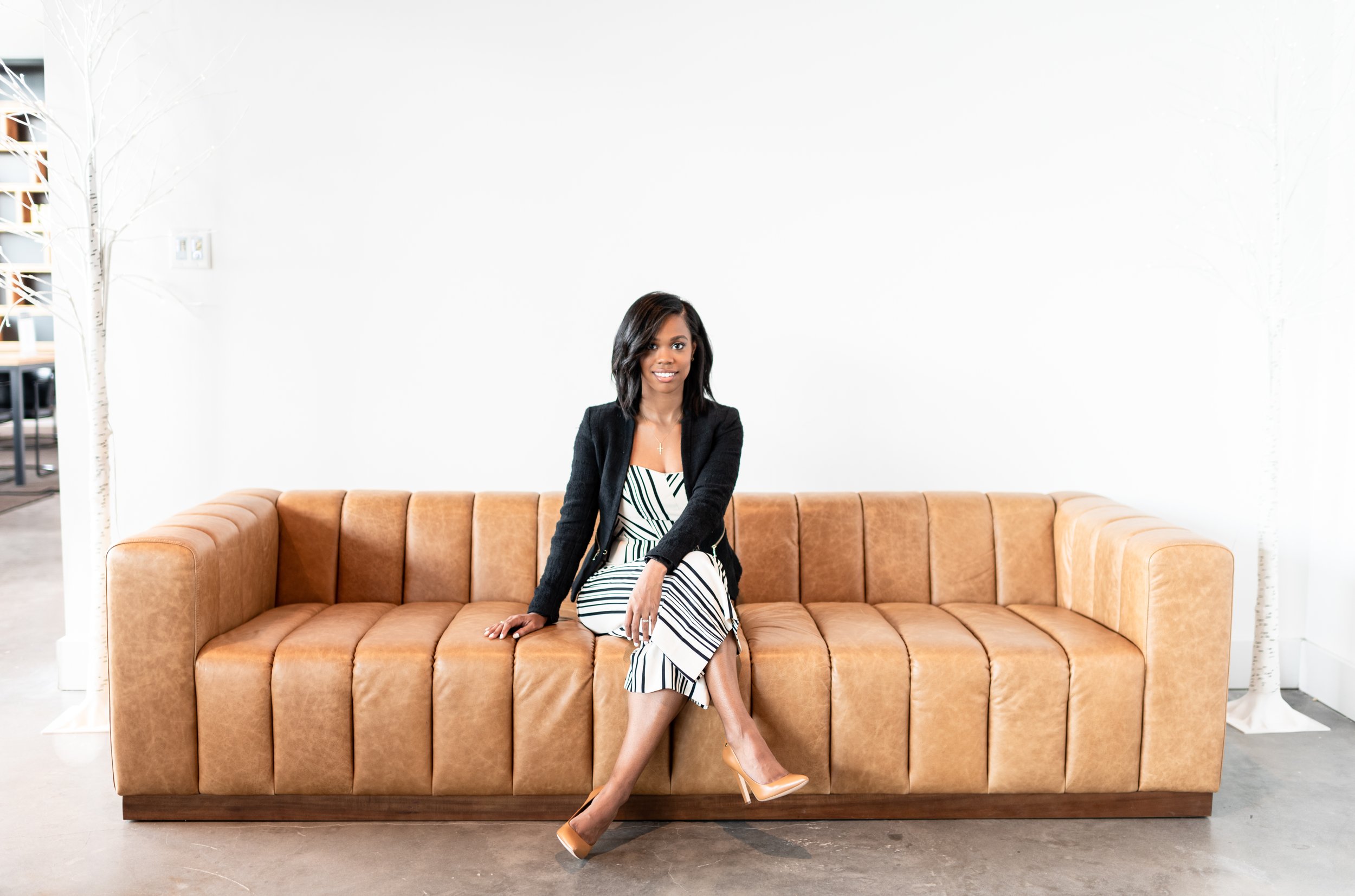 A woman sitting on a tan leather sofa against a white wall in a modern, minimalistic room.