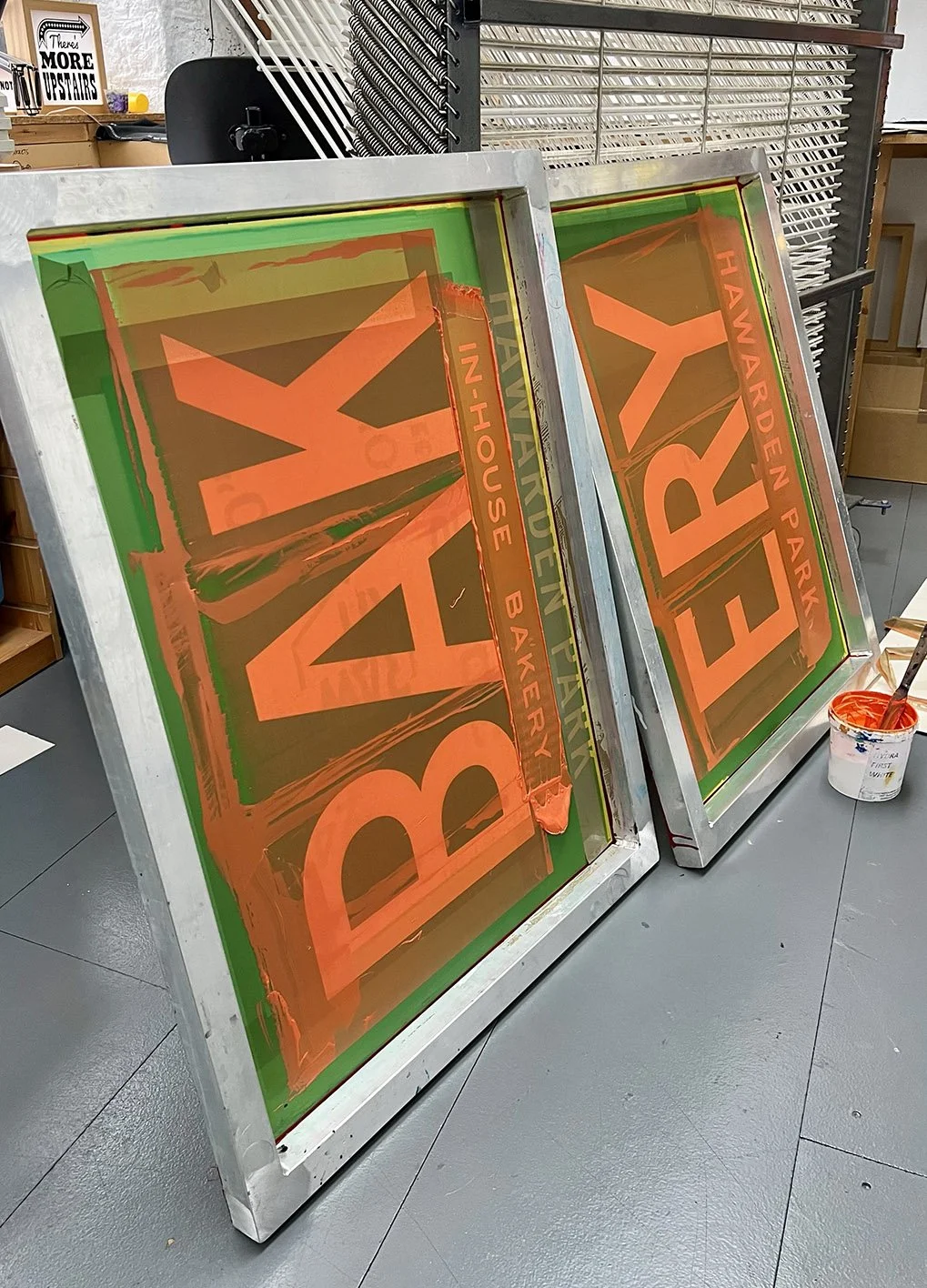 Two silk screens that read the work 'bakery' leaning against a surface, with ink pot and brush nearby in an indoor workspace.