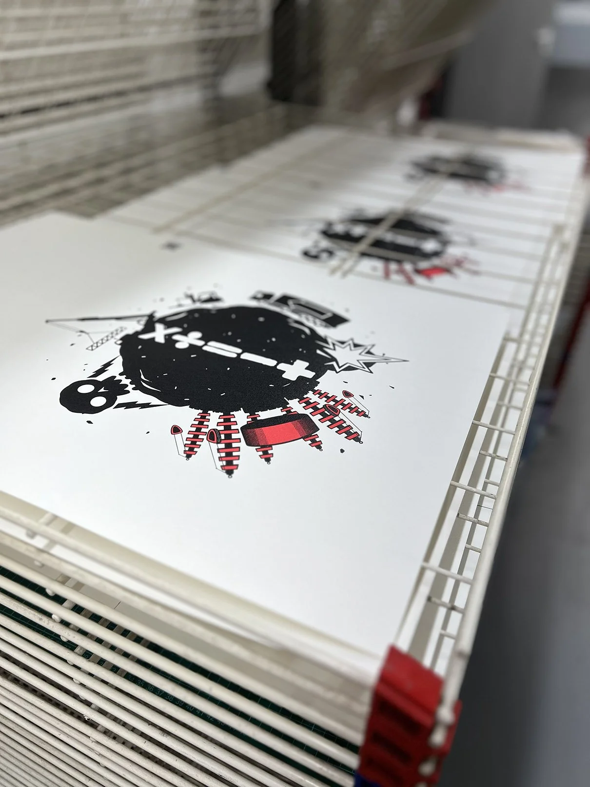 Several printed posters with a graphic of a black bomb and red and black lines, stacked on a wire shelving unit for Pots & Pans Productions.