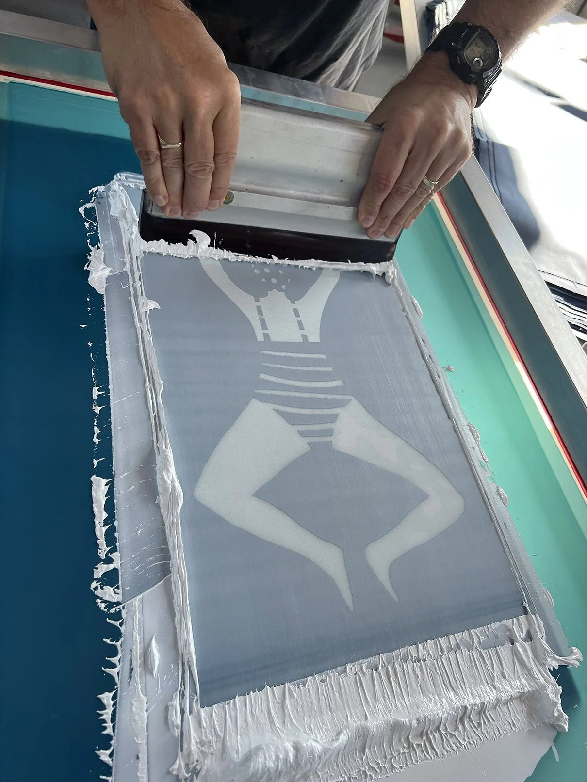 A person screen printing a design onto fabric, with the person's hands pressing a squeegee over the fabric. The design appears to be a stylized figure with an angular shape.
