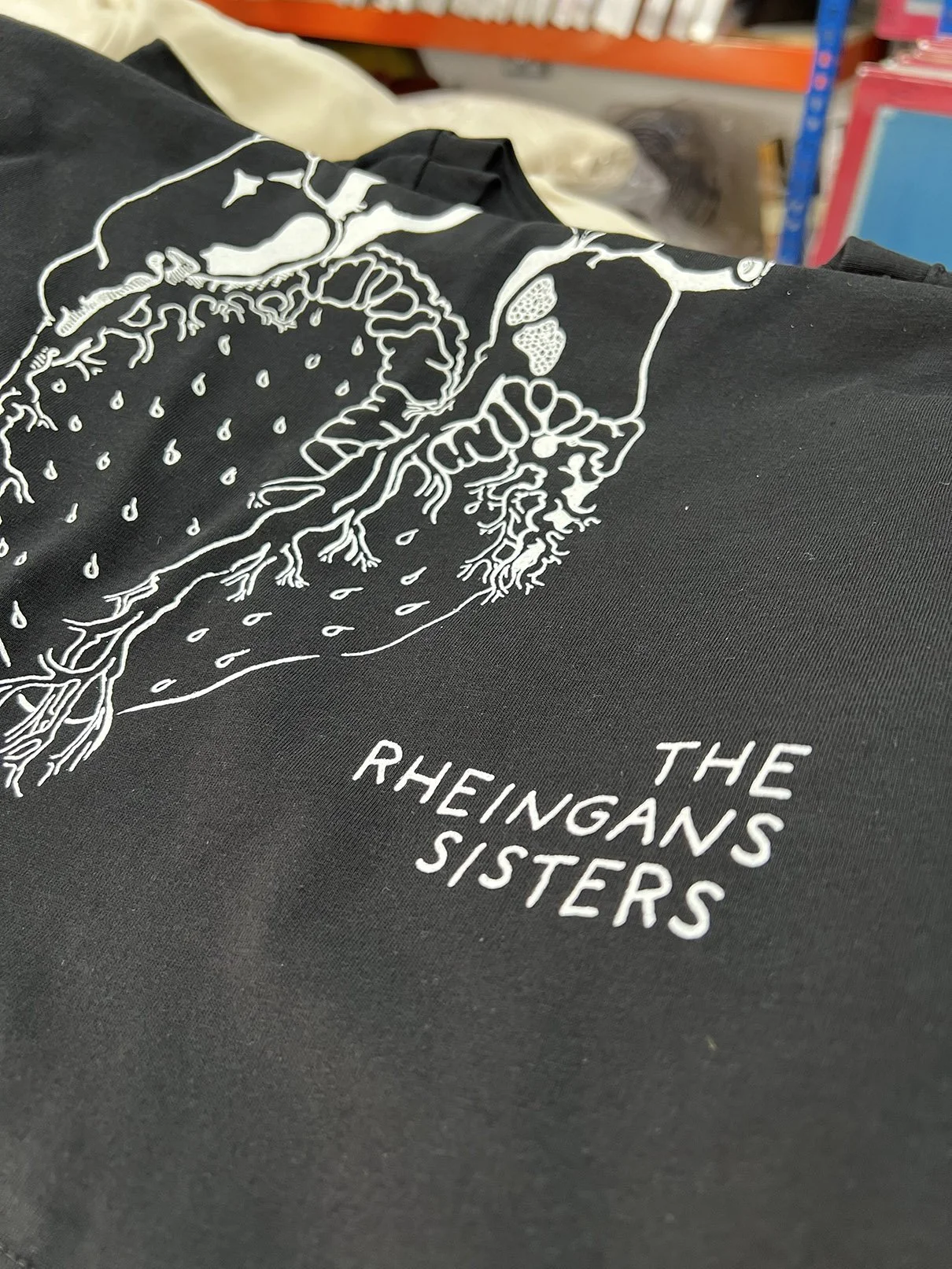 A black T-shirt with a white illustration of the human digestive system and the text 'The Rheingans Sisters' underneath.