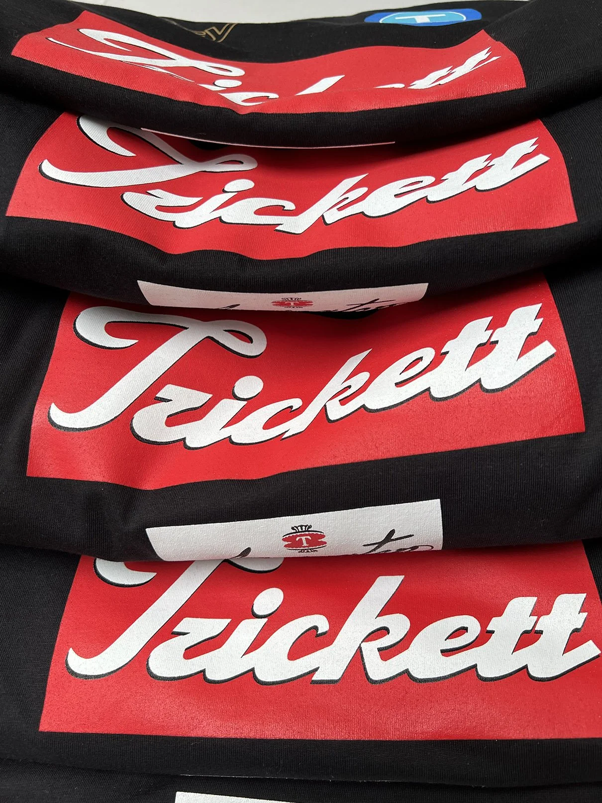 Stack of black T-shirts with red and white 'Tickett' logo printed on them.