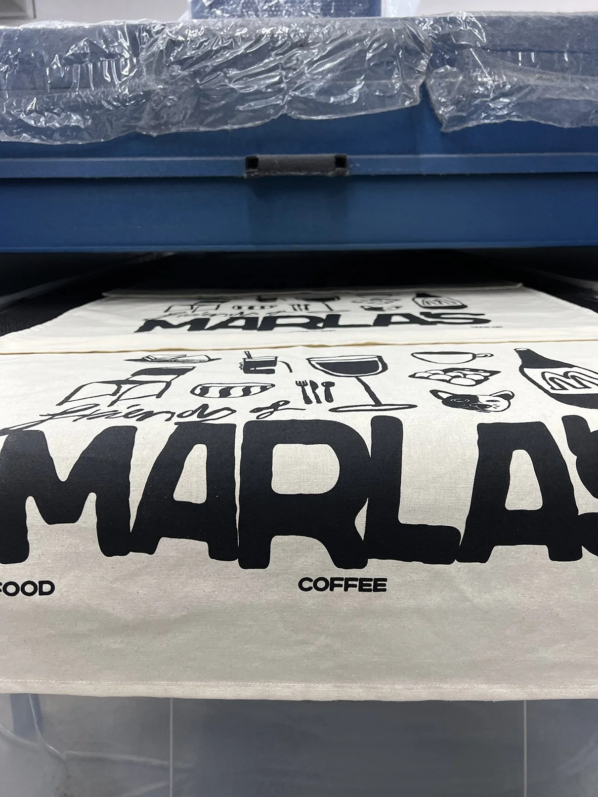 Close-up of a teatowel for Marlas Sandwich Shop in Hull, with various illustrations and text related to food and coffee on a white background.