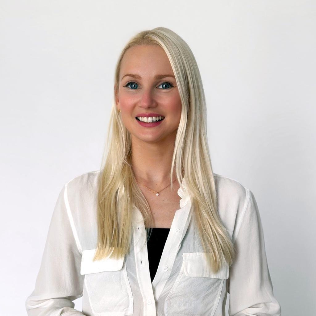 En ung kvinna med långt blont hår, blå ögon och vit skjorta, som ler mot kameran.