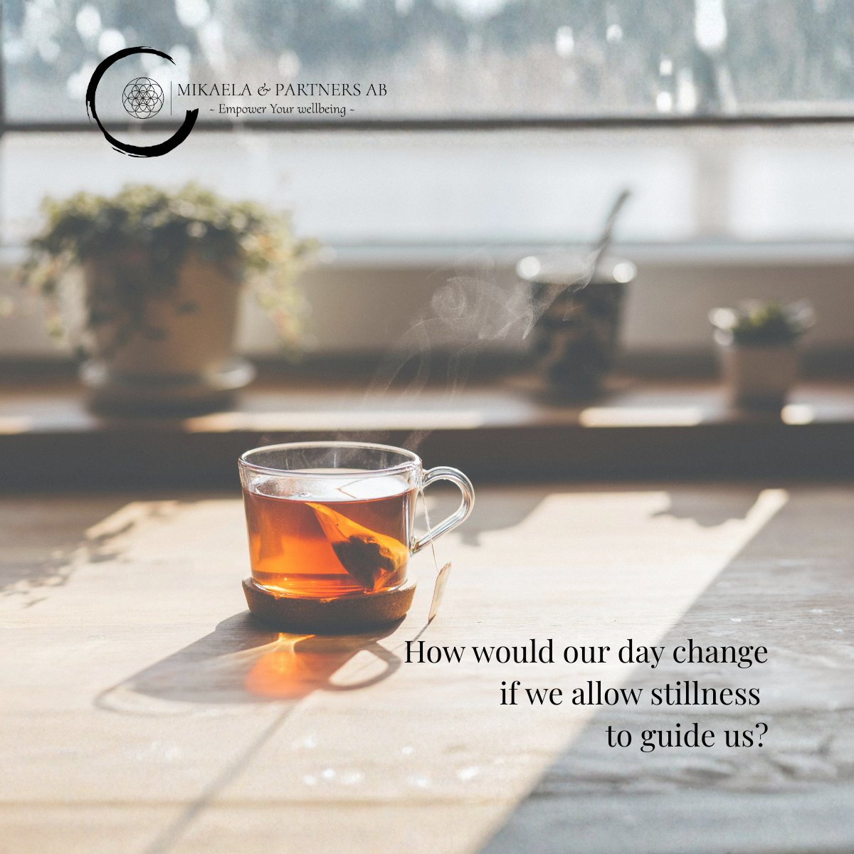En kopp te på ett träbord med solljus som skiner genom ett fönster, bakgrund med växter och ett vykort eller bok. Text på bilden: "How would our day change if we allow stillness to guide us?" samt logotyp för Mikaela & Partners AB.