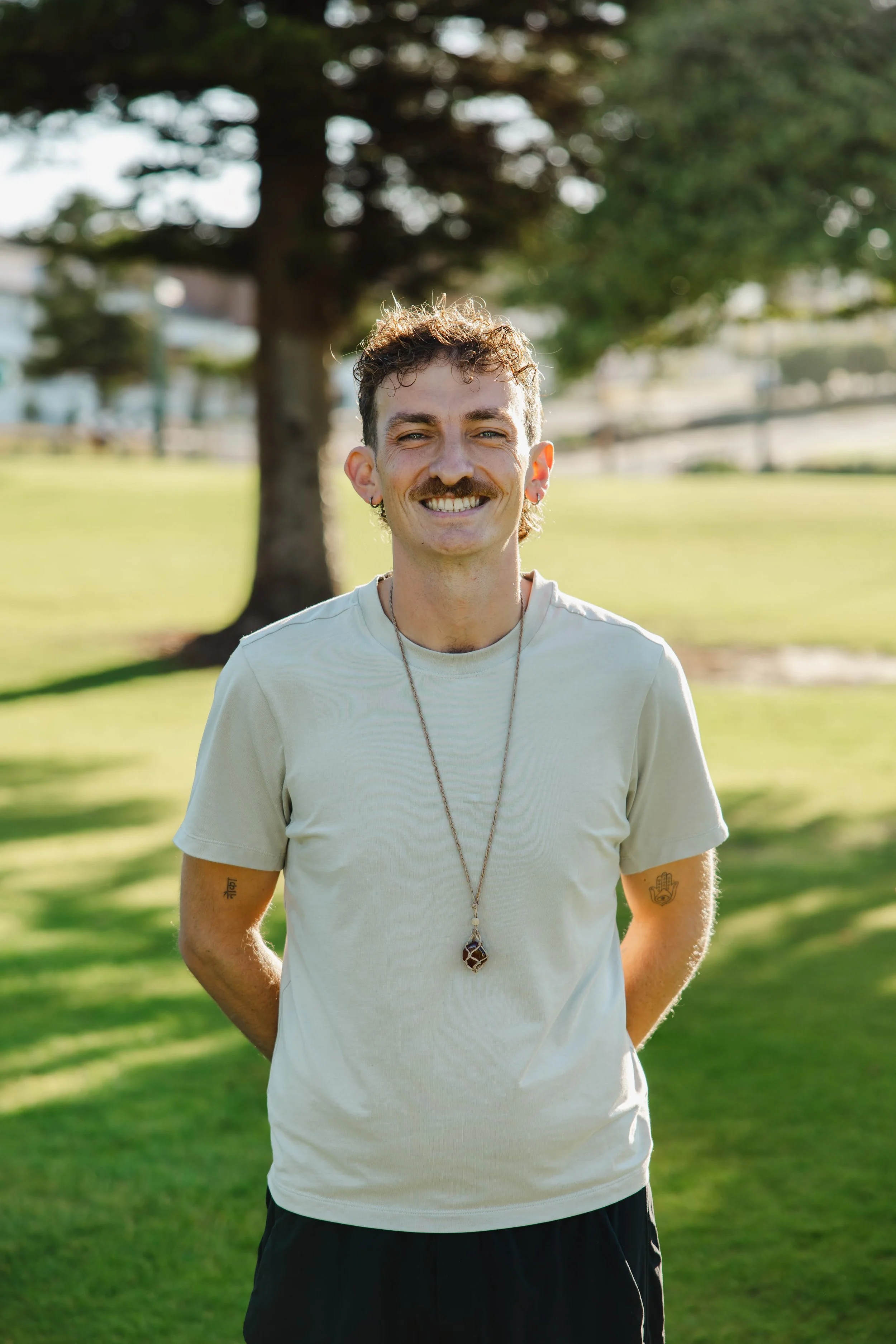 Front picture of male wearing a necklace in a background of trees and grass