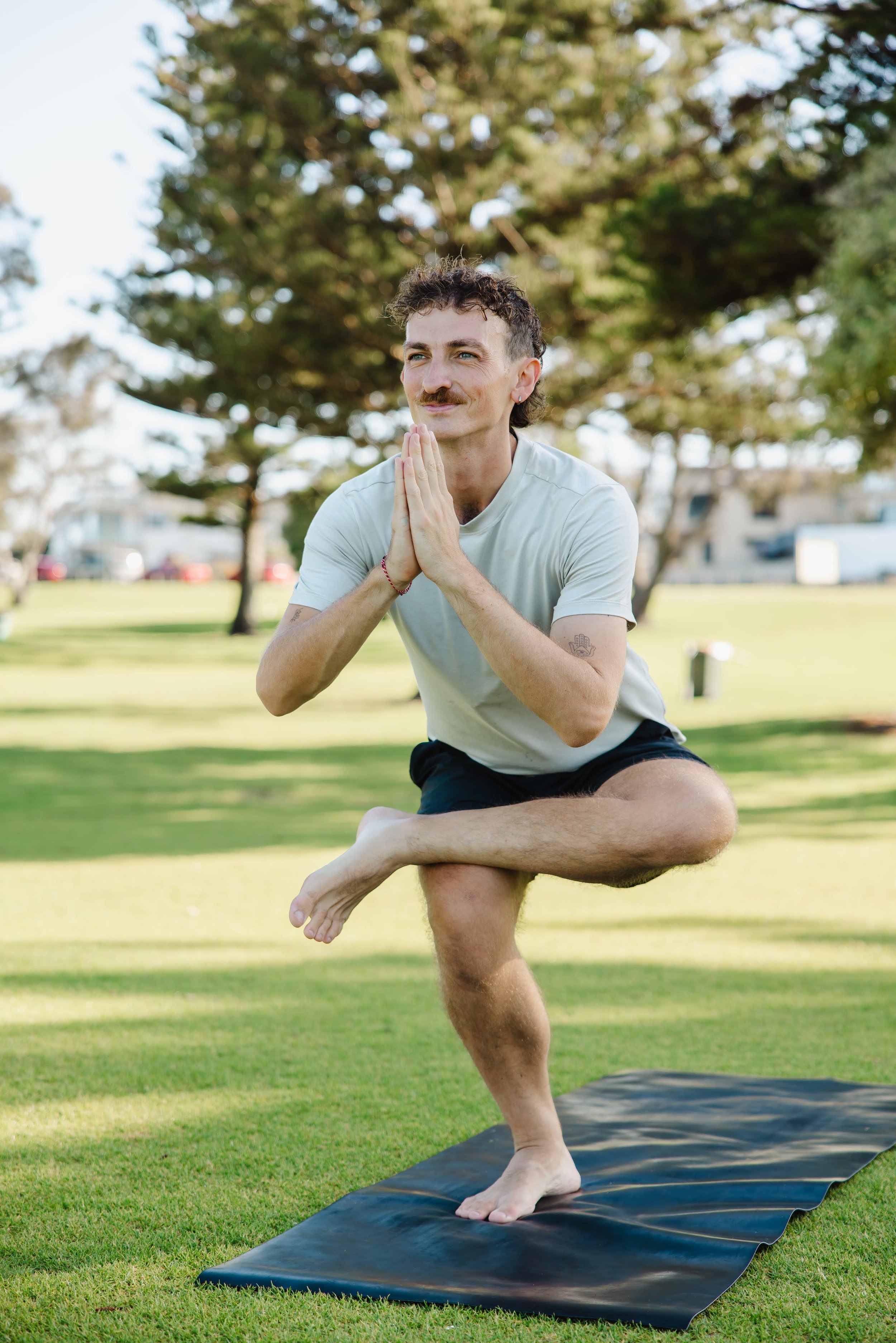 Male posing in a yoga pose on a mat against a backdrop of grass and trees