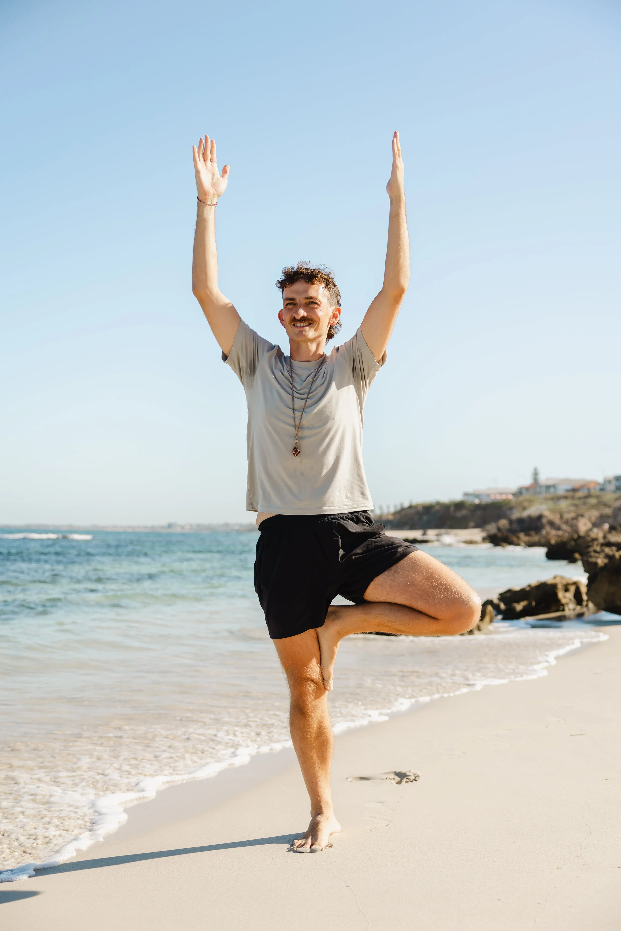 Male posing in tree pose against a backdrop of the beach