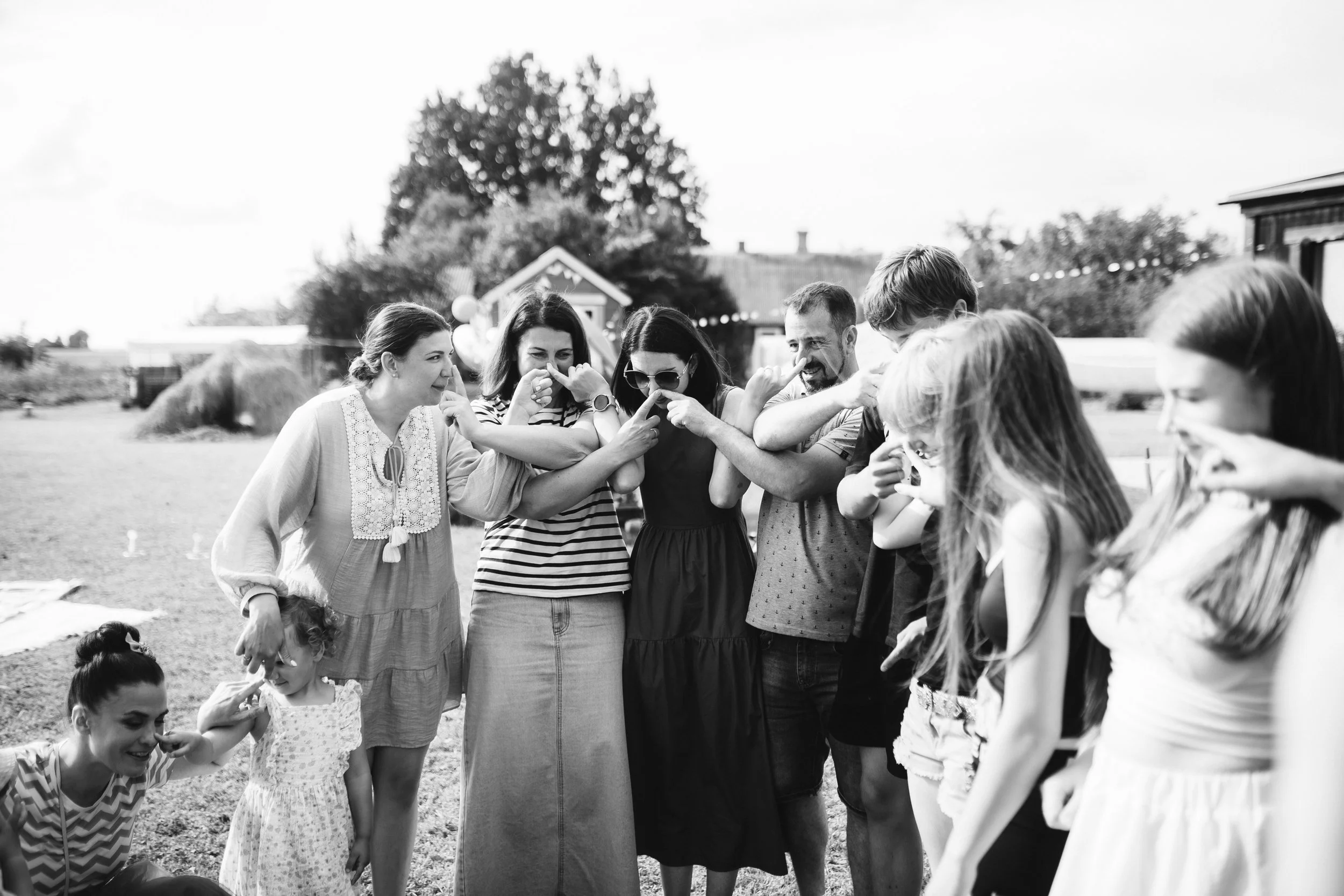 Group of people laughing and playing together outdoors in a sunny yard, with a small house and trees in the background.