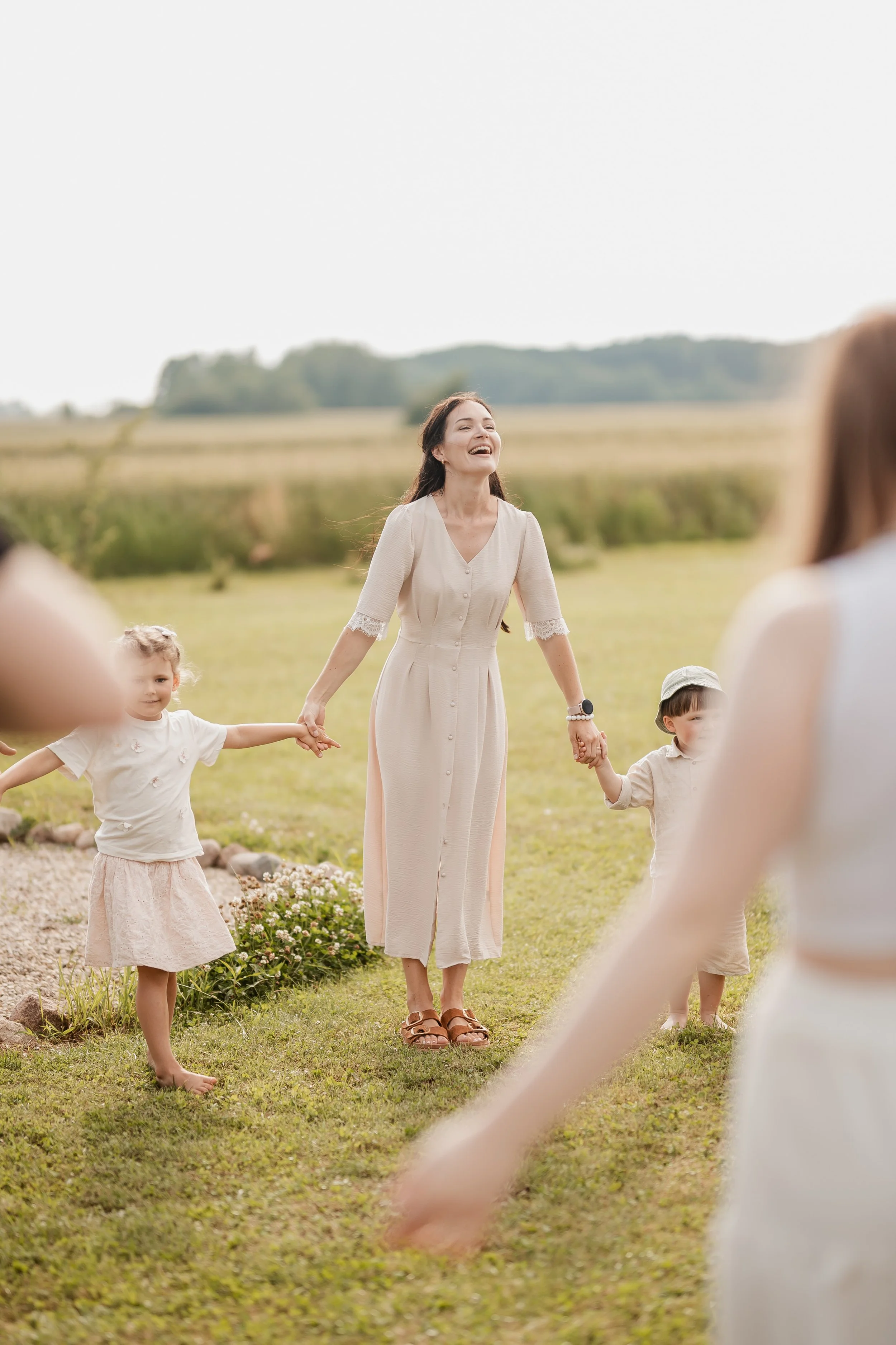 Woman holding hands with two children and smiling while standing in a grassy field with mountains in the background.