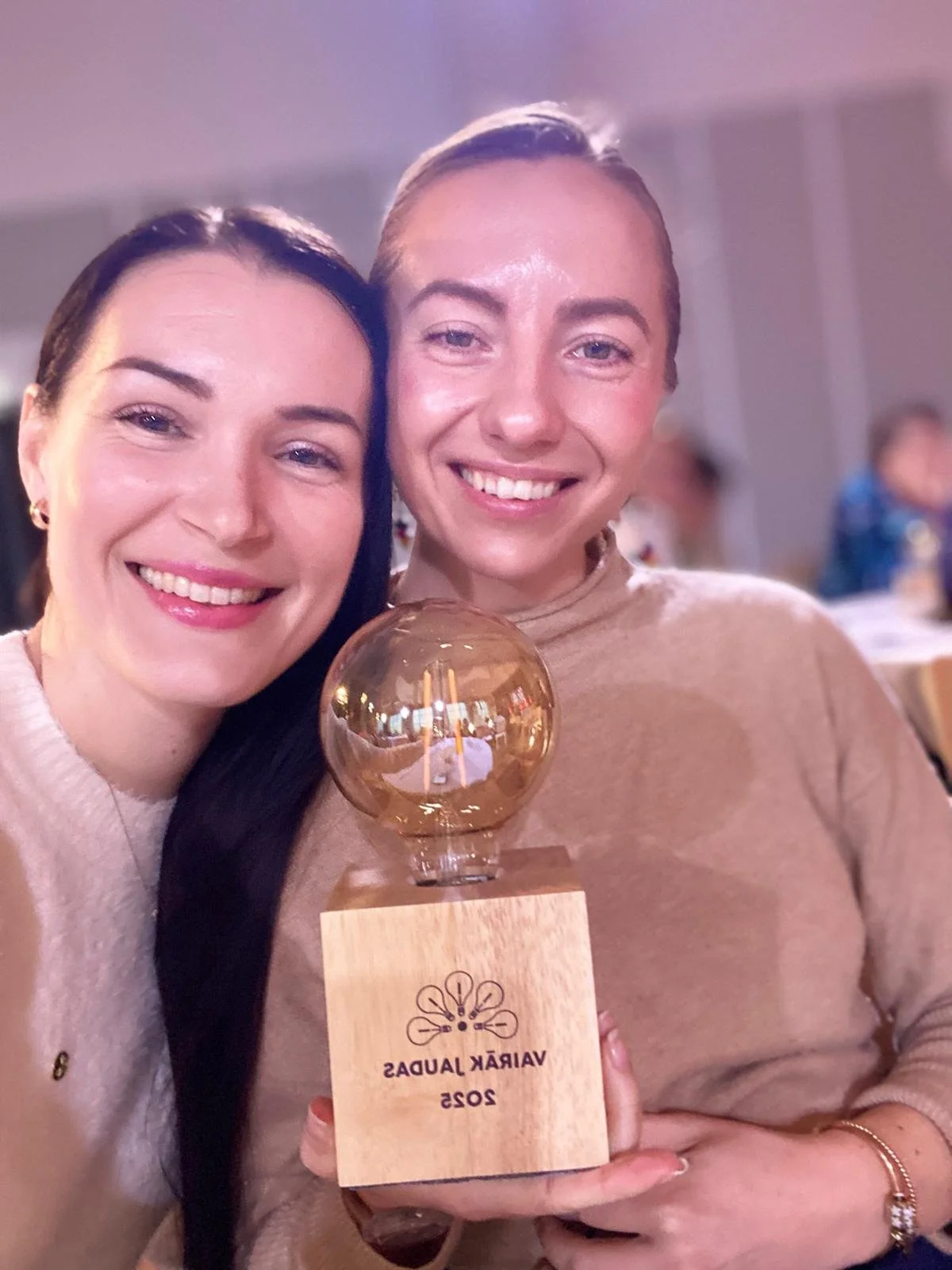 Two women smiling and holding a trophy with a wooden base and a transparent globe on top, at an event labeled 'VIRÁŘEK JAUDA 2023'.