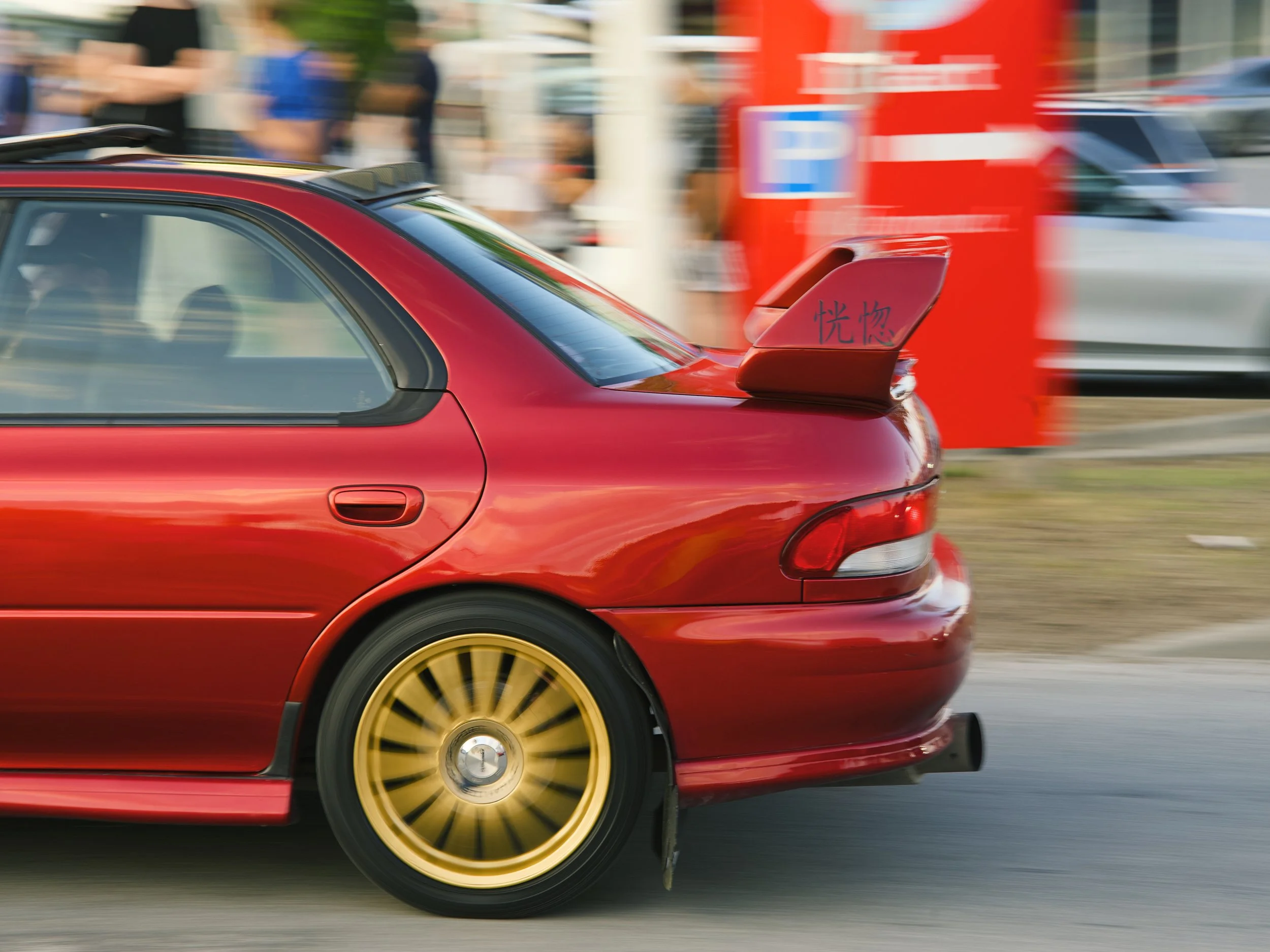 Red sports car with gold wheels driving on the street.