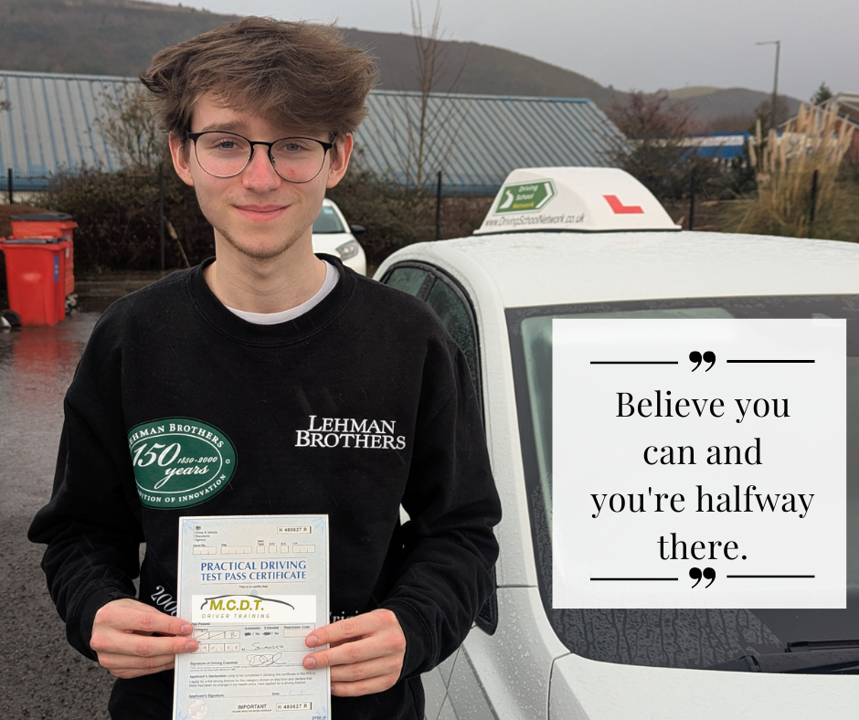 A young man with glasses and light brown hair, wearing a black sweatshirt, holding a practical driving test pass certificate standing in front of a white car with a driving school sign on top. There is a quote on the image that says, "Believe you can and you're halfway there."