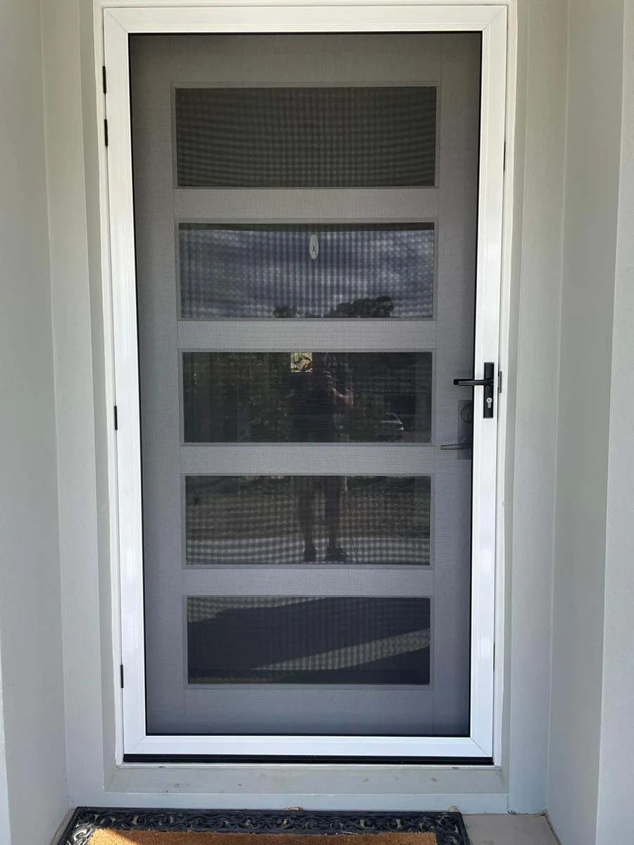 front view of a Security screen door with a white frame, black handle, installed in Gold Coast family home at Palm Beach with a brown doormat at the doorstep.