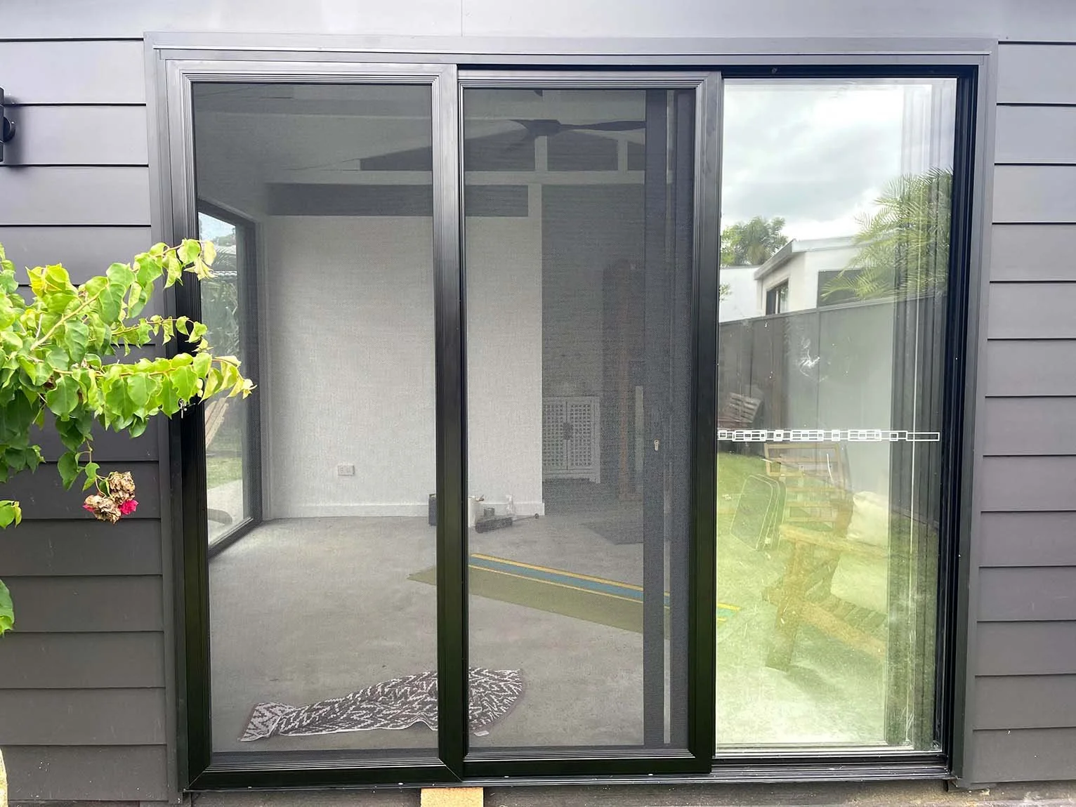 Exterior view of a black-framed sliding security door leading to an enclosed tiny home with grey walls and a carpeted floor. Screenguard security door installed by Hinterland Screens Gold Coast.