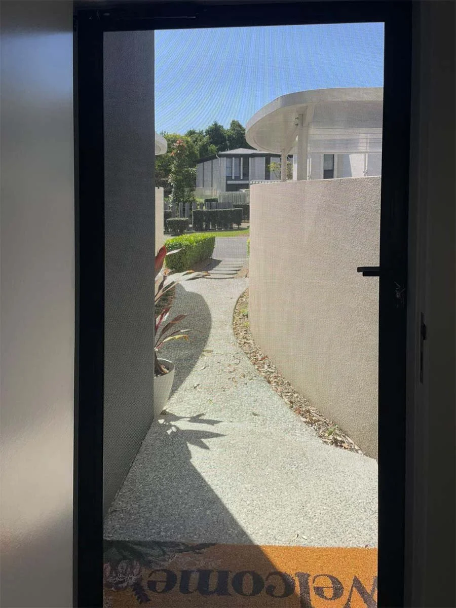 View through a Stainless steel security screen door in a Gold Coast home. Can see driveway and outdoors in bright sunlight.