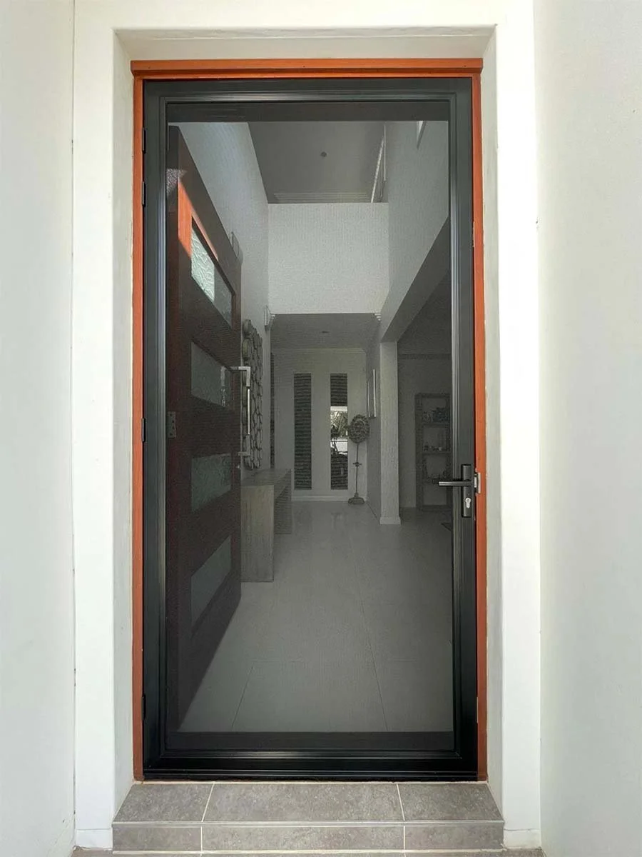 A black framed security door with a wooden trim, leading into a modern interior with white walls and tiled flooring. Terranora home.