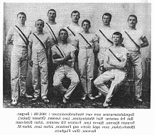Bildet viser en gruppe på ti mannsporttere iført gamle baseballuniformer, noen med baseballkøller, poserende for et gruppebot utenfor.
