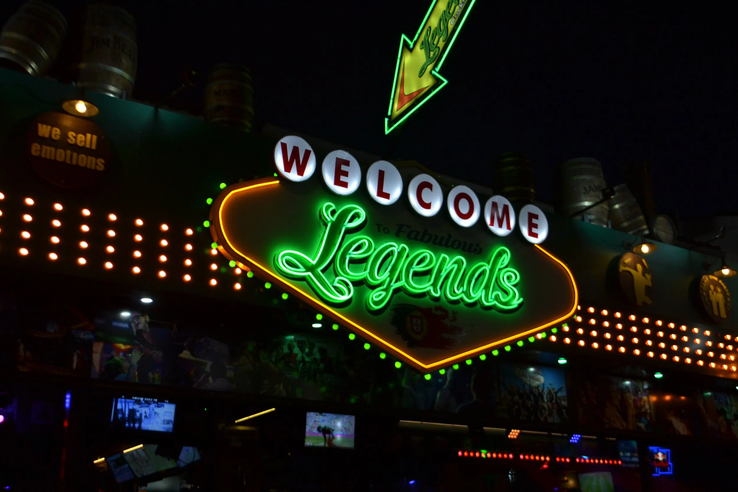 Neon sign at night reading 'WELCOME to Fabulous Legends' with colorful lights and overhead barrels.