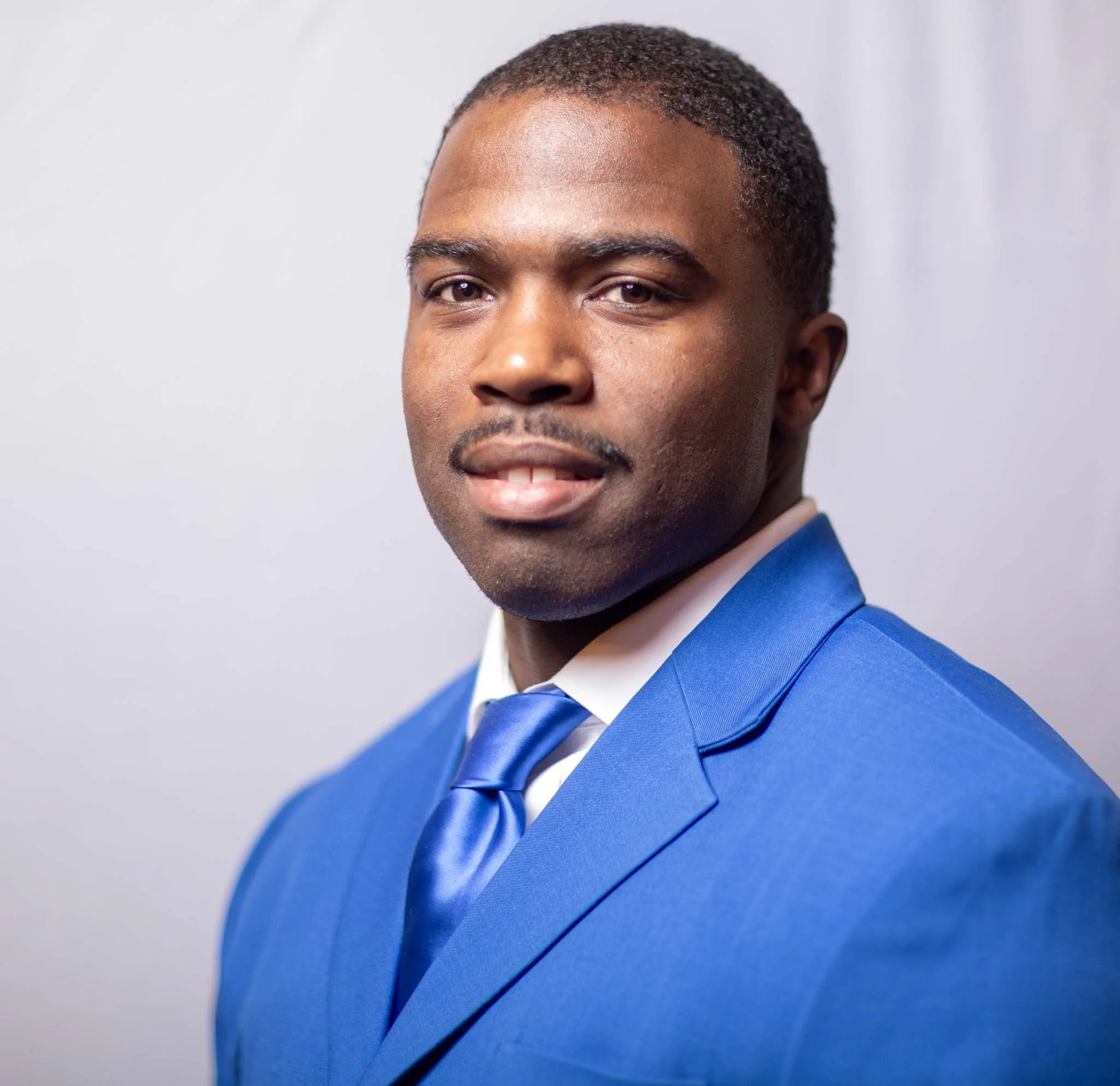 Professional Black man in a blue suit and tie posing against a light background.