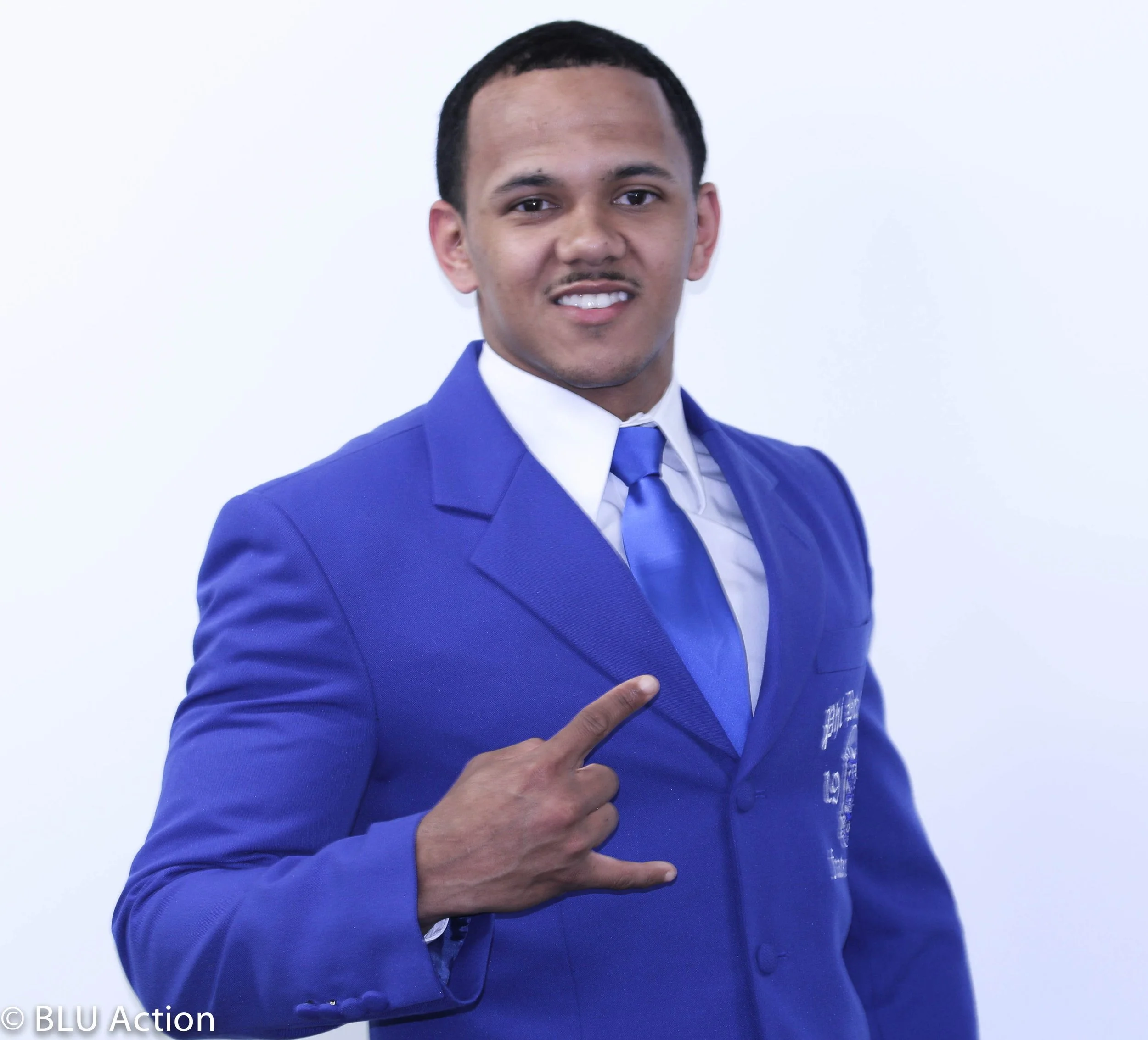 Young man in a blue suit and tie smiling and making a rock on gesture with his right hand.