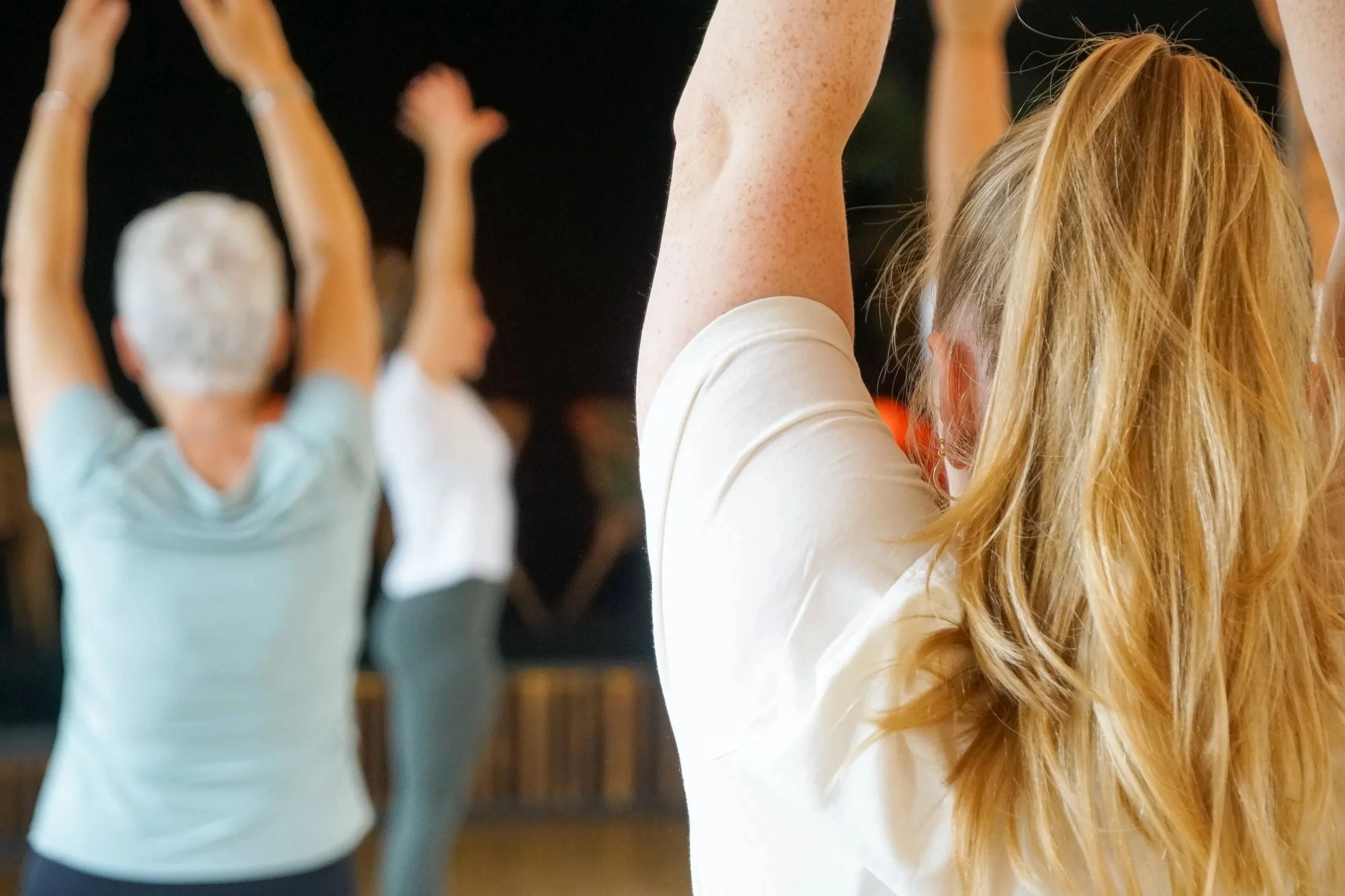 Menschen, die Yoga oder Meditation im Raum praktizieren, mit Fokus auf eine Frau mit langen, roten Locken.