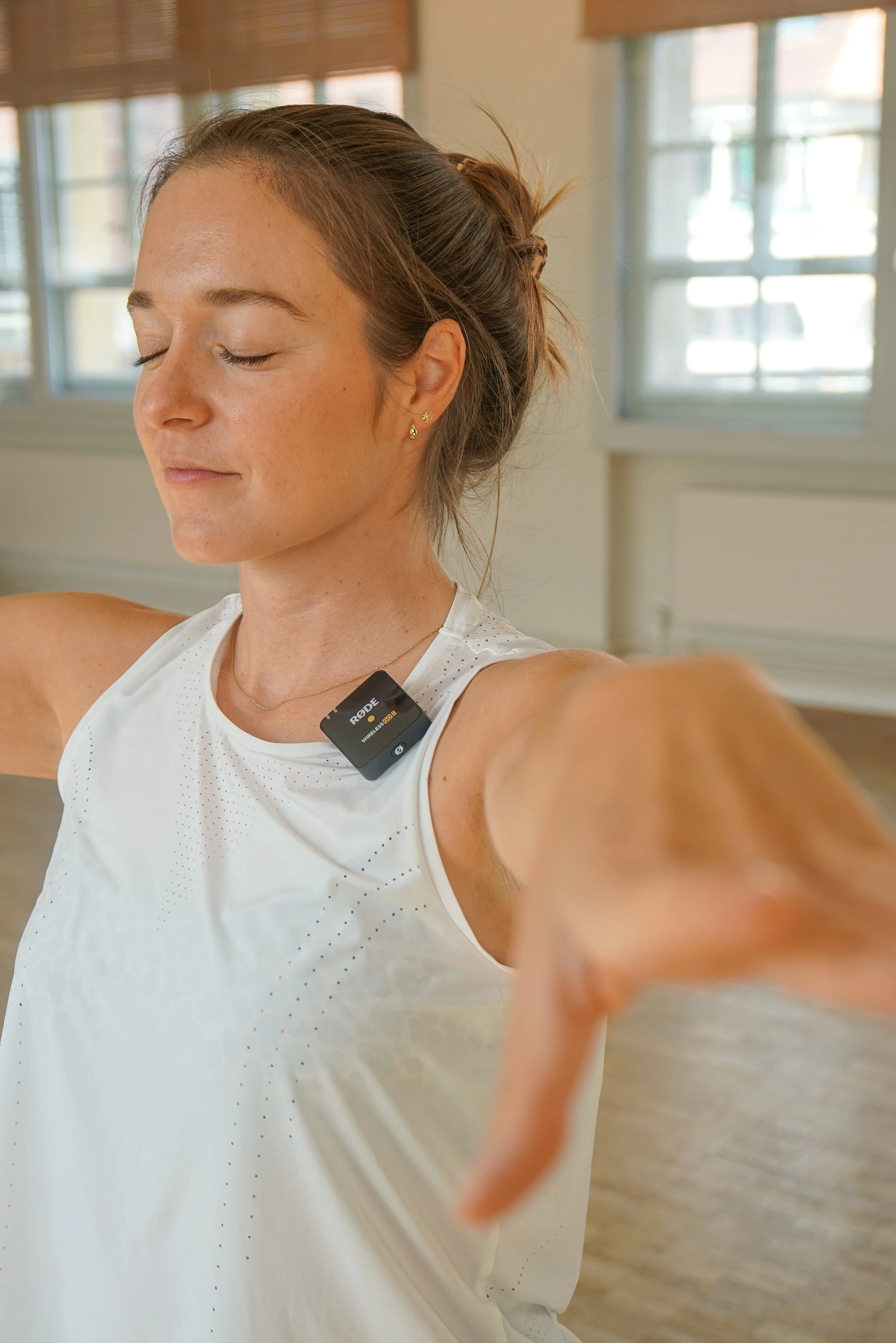Nahaufnahme eines Mannes beim Yoga im Fitnessstudio, mit offener Haltung und entspanntem Gesicht, trägt weiße Sportkleidung und ein Funkmikrofon am Hals.