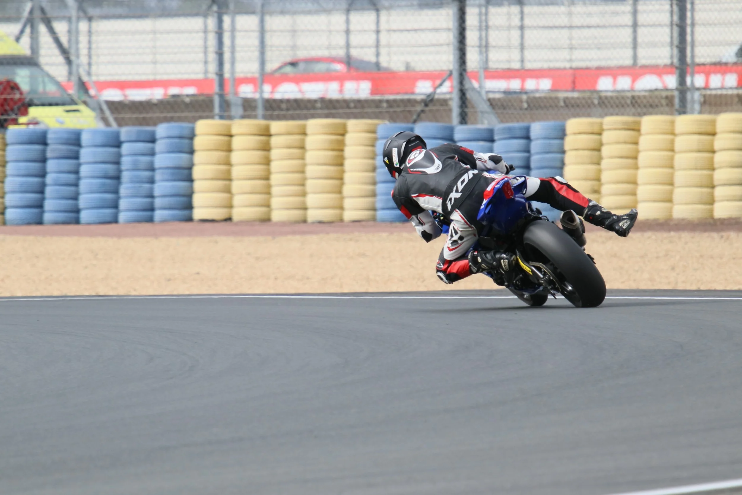 Un pilote de moto en train de prendre un virage sur une piste de course, portant un équipement de protection noir, blanc, rouge et un casque noir.