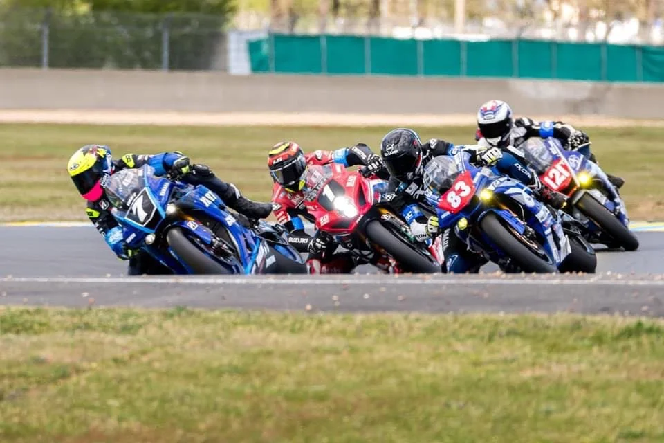 Cinq motards en course, tournant en virage serré sur une piste de motocyclisme.