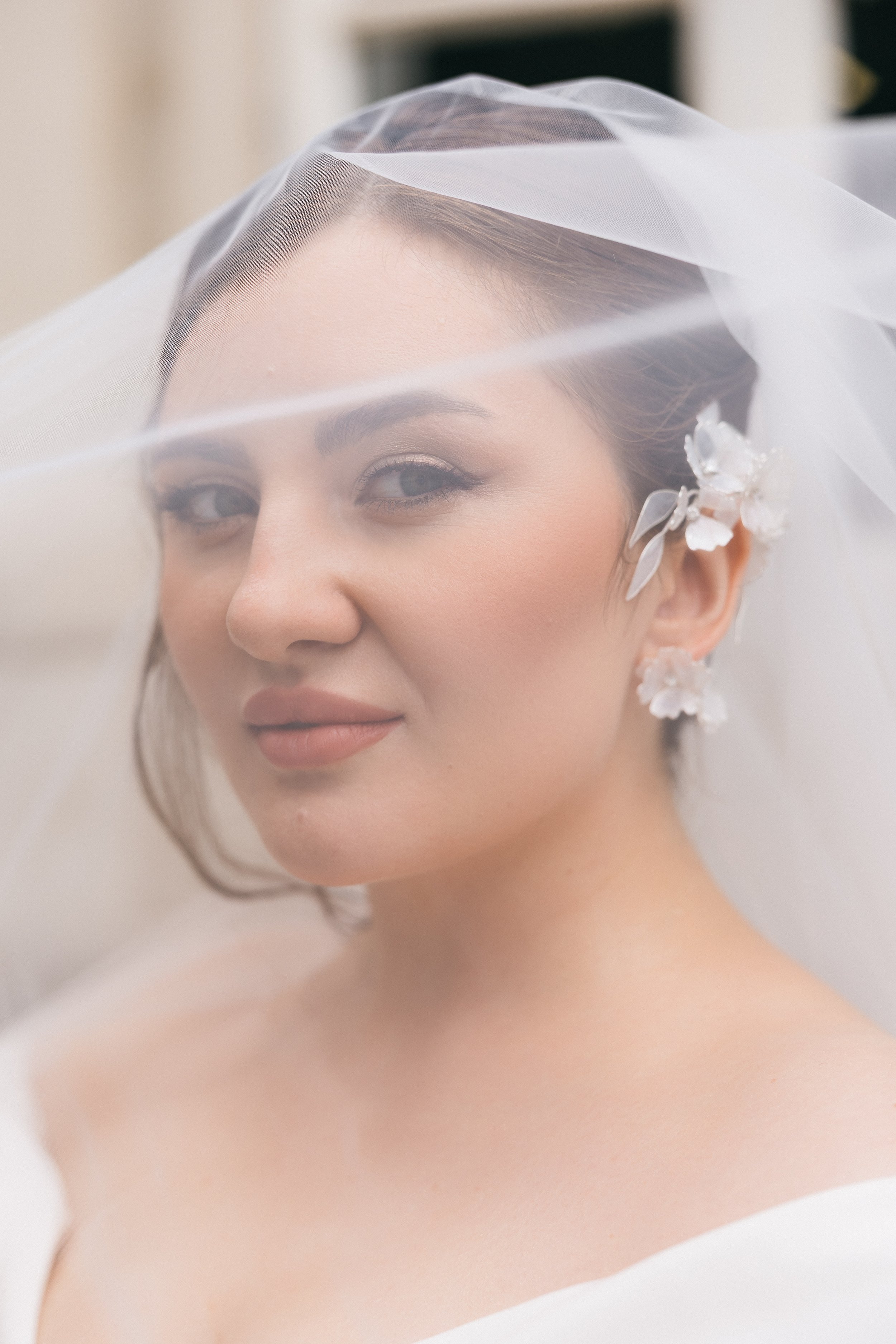 A close-up of a bride with a veil and floral earrings looking at the camera.