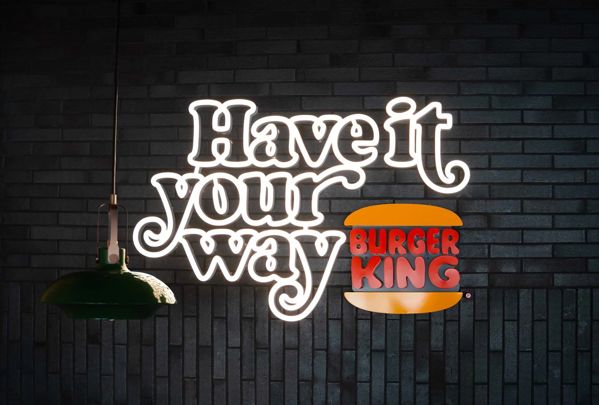 Neon-Schild mit der Aufschrift "Have it your way" und dem Burger King Logo vor einer schwarzen Ziegelwand.