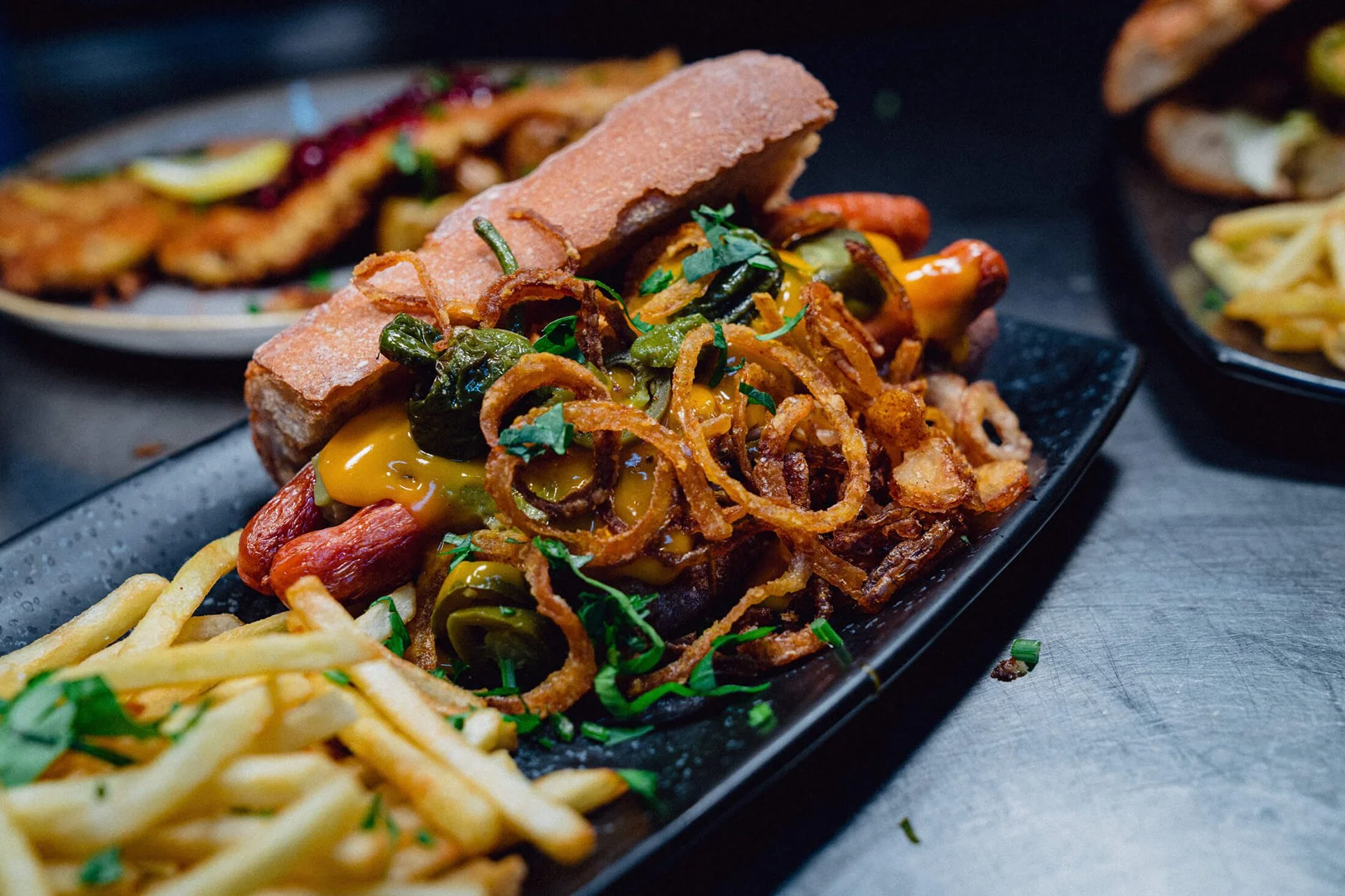 Ein Teller mit einem Sandwich, Pommes frites und frittierten Zwiebelringen, garniert mit Kräutern.