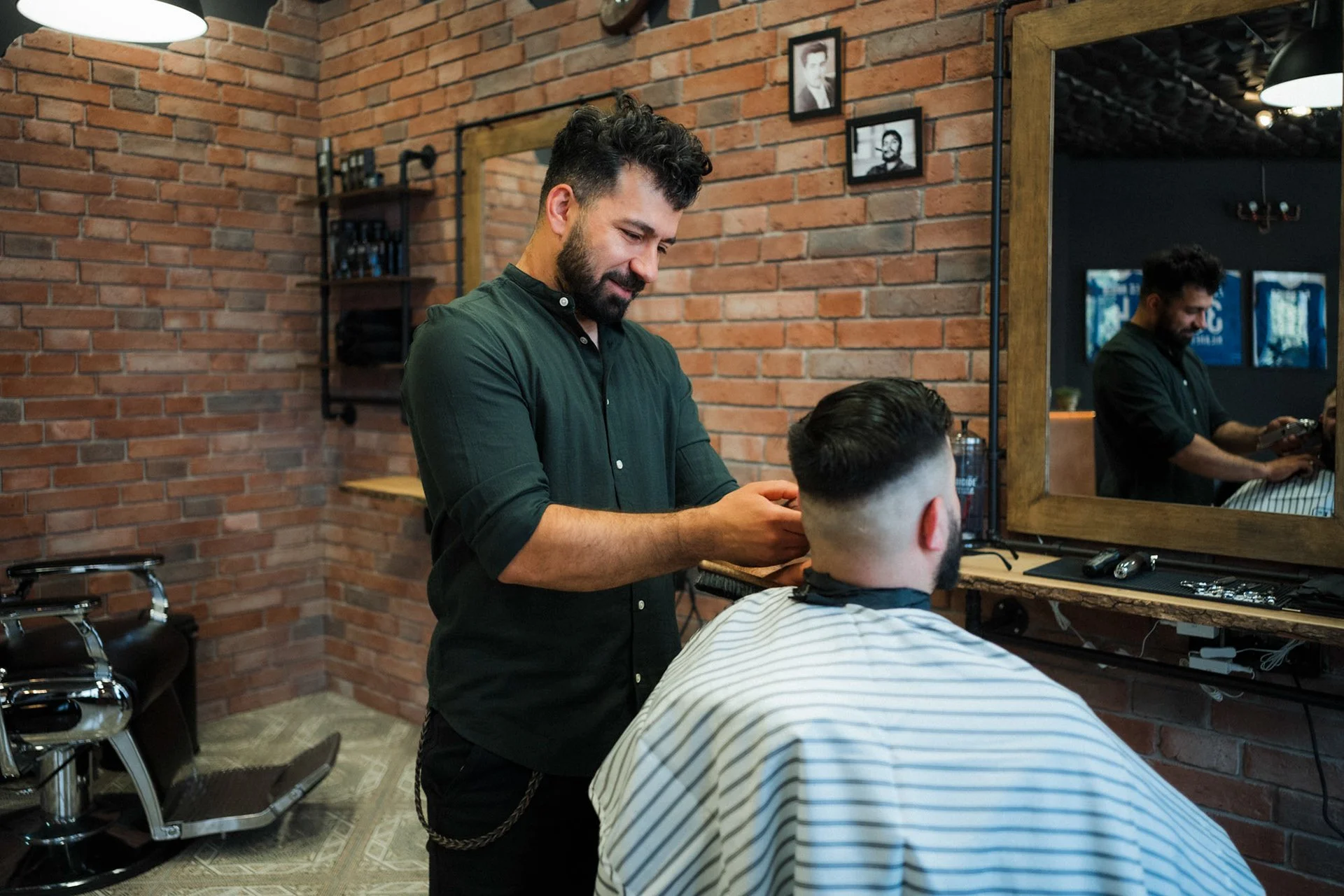 Barbier schneidet einem Kunden die Haare in einem Friseursalon mit Backsteinwänden, Spiegel und moderner Einrichtung.