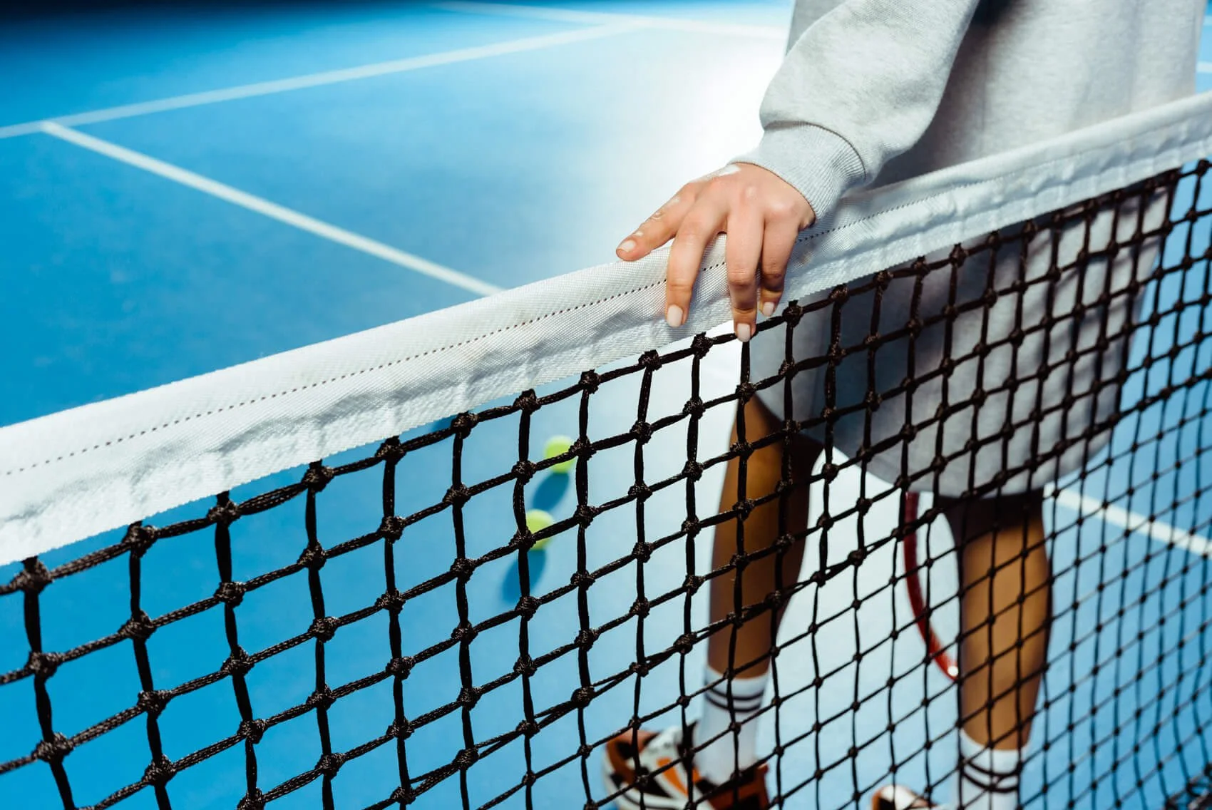 Nahaufnahme eines Tennisspiels auf einem blauen Tennisplatz, eine Person in Sportkleidung greift nach dem Netz.