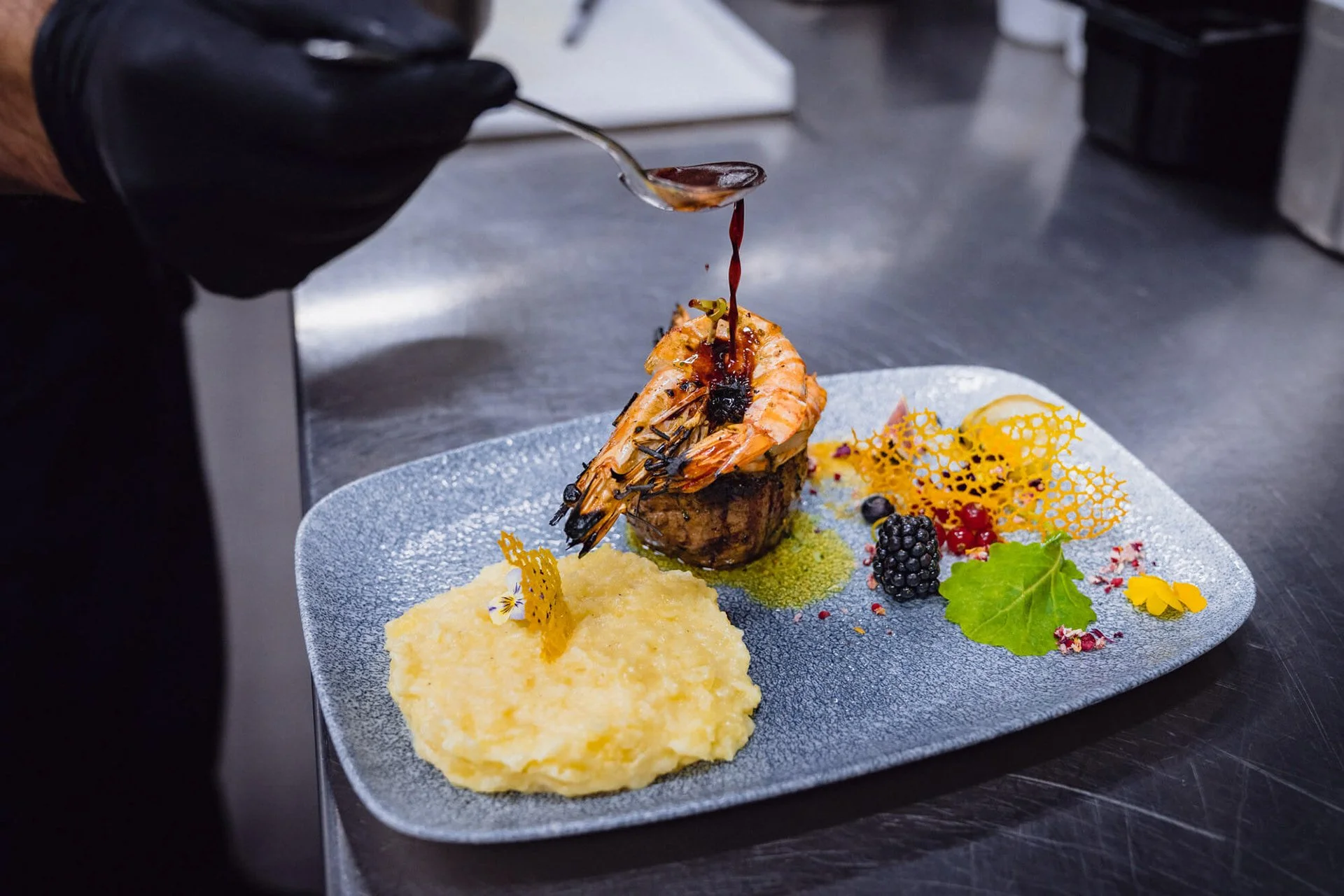 Ein plated Gericht mit Meeresfrüchten, Kartoffelpüree und Dekorationen, bei dem eine Person eine Soße auf die Meeresfrüchte träufelt.