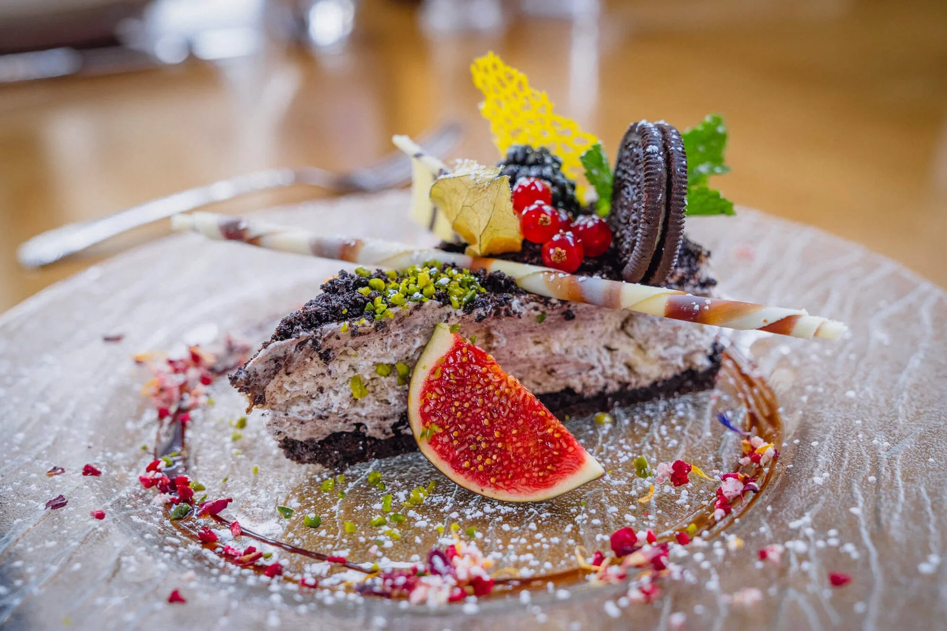 Ein Stück Torte mit verschiedenen Dekorationen wie Orangenscheibe, Oreo-Kekse, Beeren, Minzblätter und essbare Verzierungen auf einem Puderzucker bestäubten Teller.