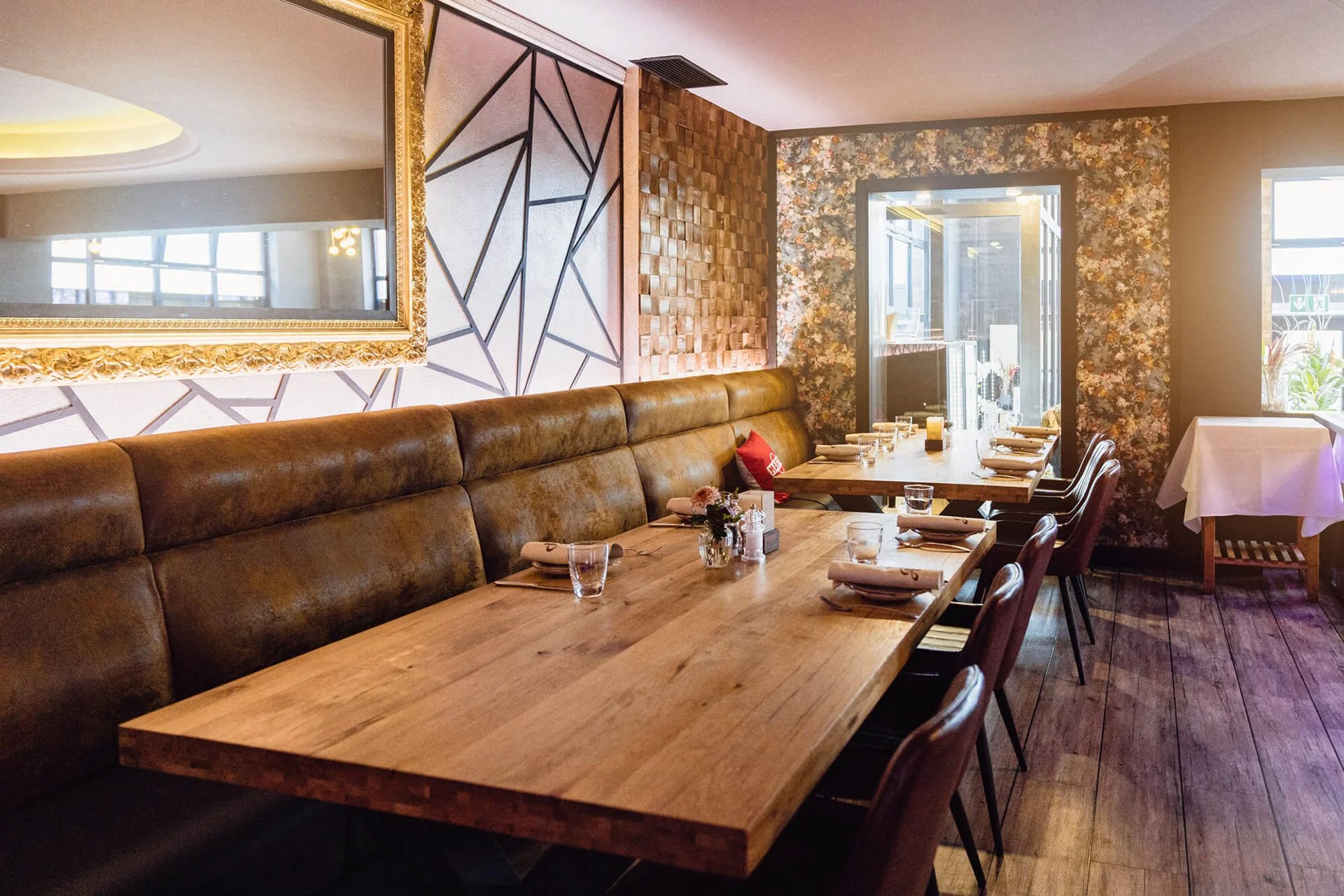 Ein gemütlich dekorierter Restaurantraum mit Holztischen, braunem Leder-Vorgurkissen, Wandverzierungen und Blumendekor.