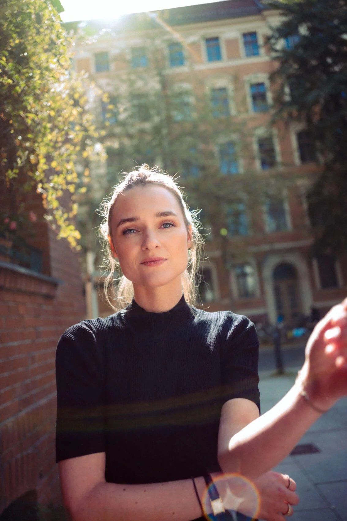 Josephin Busch beim Fotografieren im Freien, Sonnenlicht, Stadtgebäude im Hintergrund.
