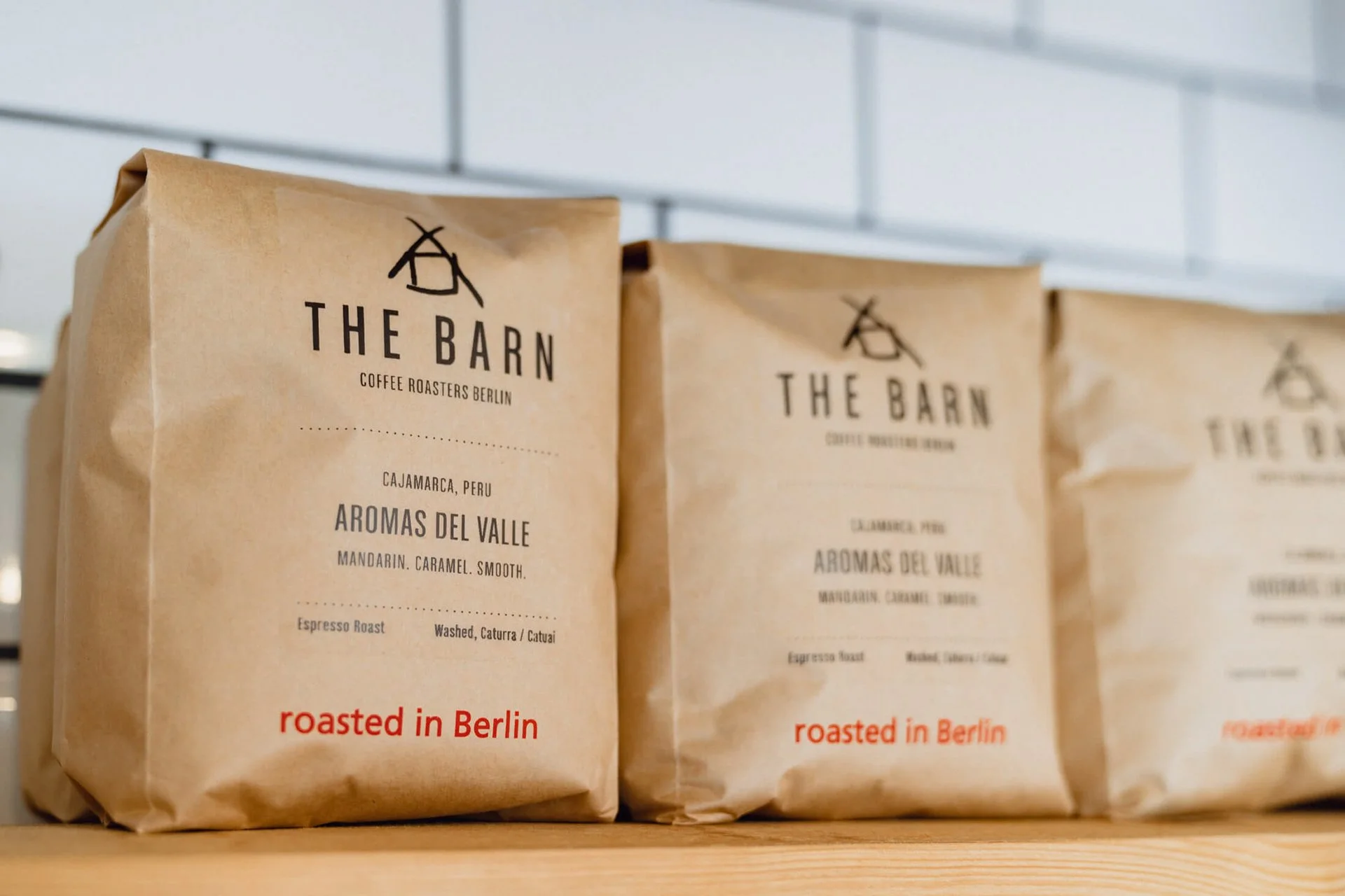Kaffeepackungen von 'The Barn' auf einem Regal, mit dem Text 'roasted in Berlin' in rotem Schriftzug.
