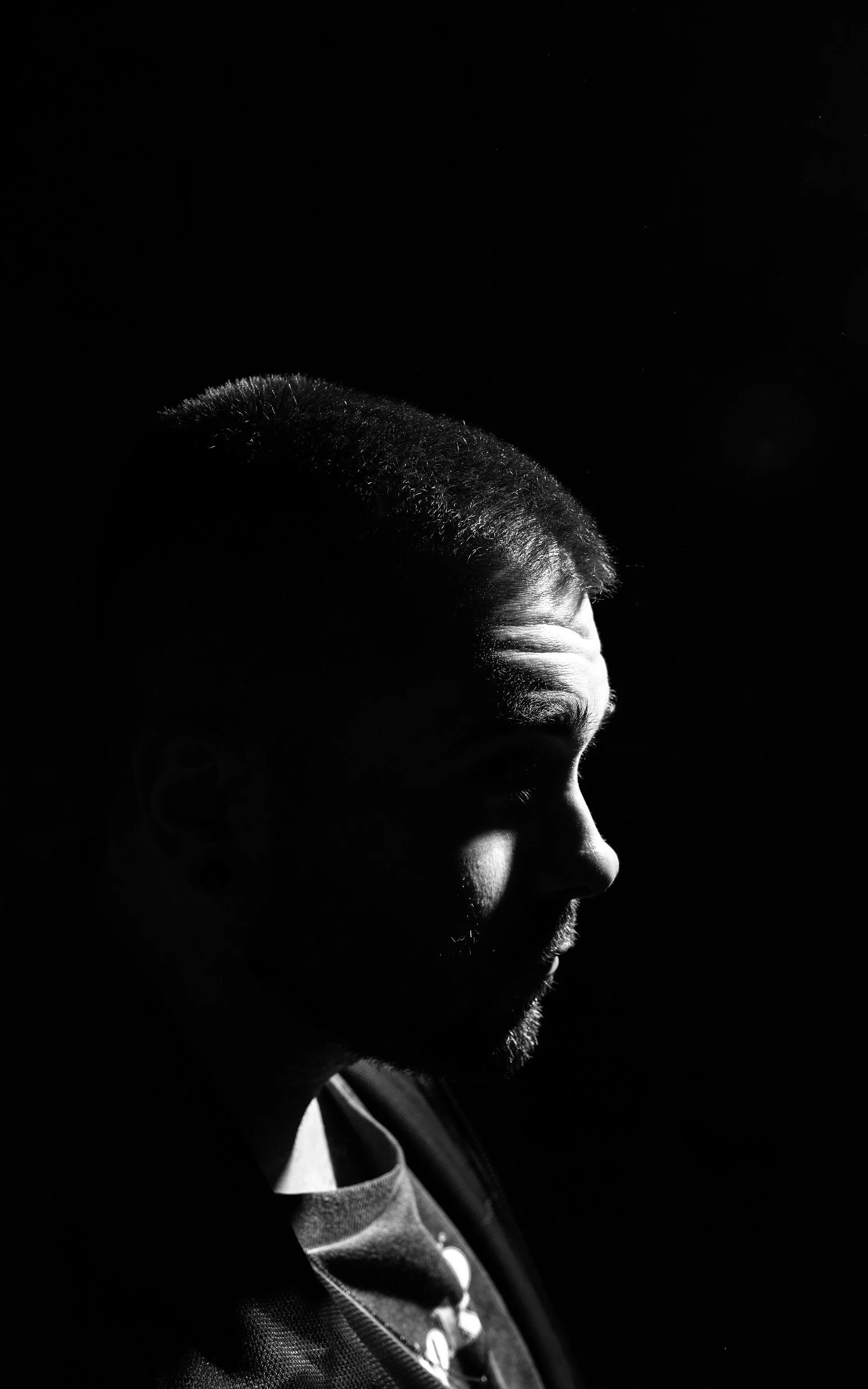 VAU schwarz-weiß-Porträt in Profilansicht mit starkem Kontrast, der nach rechts blickt, vor dunklem Hintergrund.