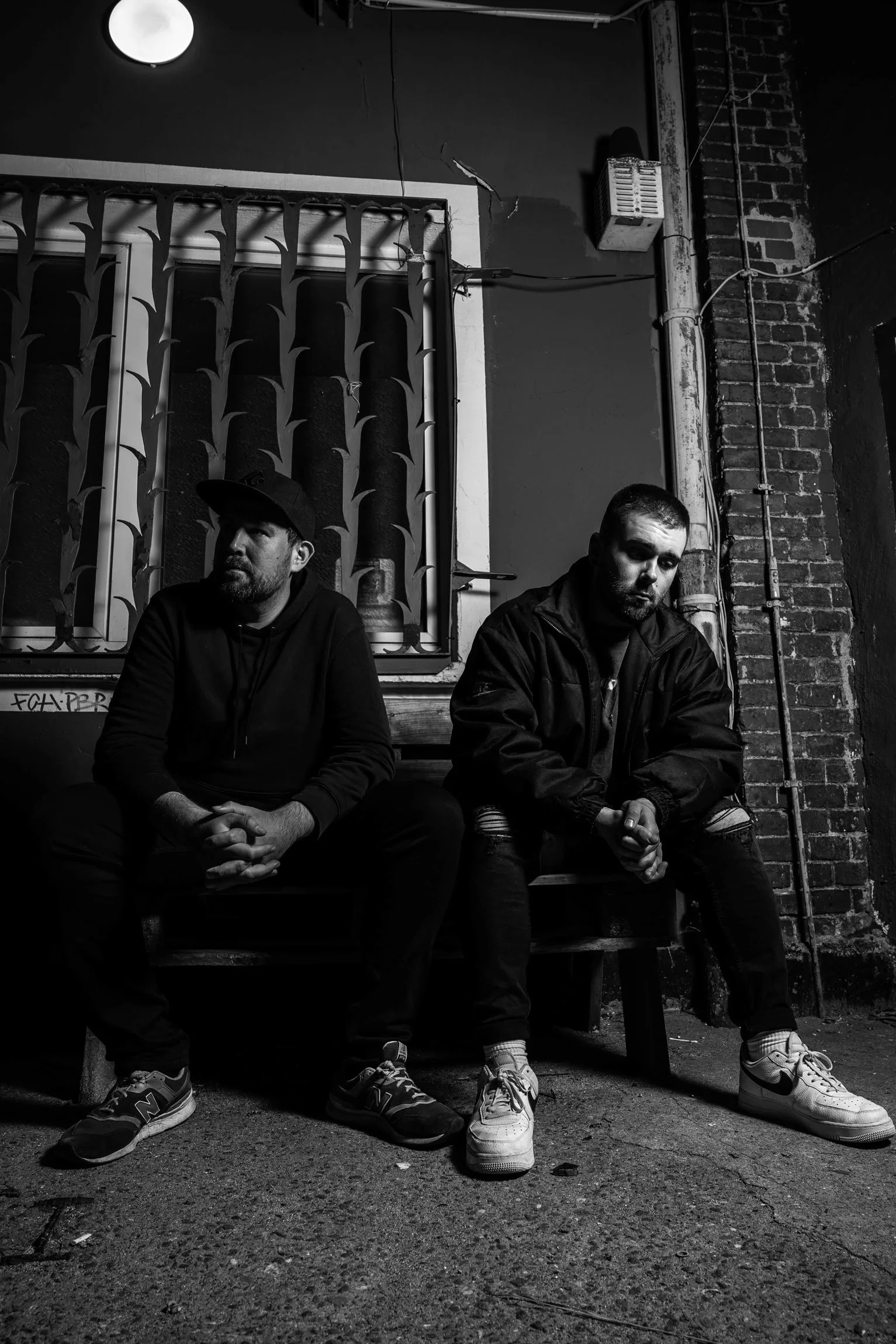 Zwei Männer sitzen auf einer Bank in einer dunklen, urbanen Umgebung, schwarz-weiß Fotografie.
