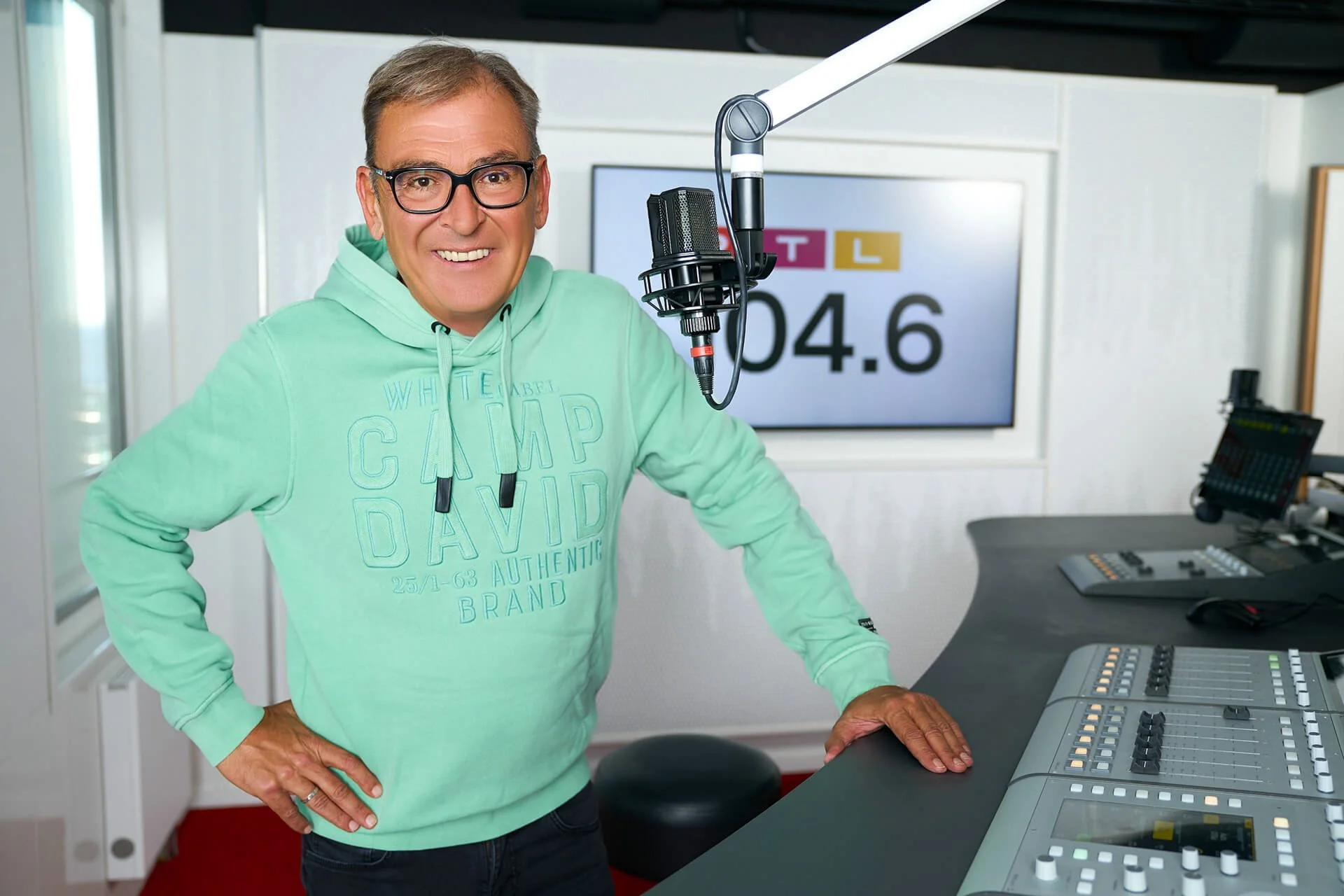 Arno Müller im Aufnahmestudio vor einem Mikrofon und Mischpult, lächelnd in die Kamera schauend.