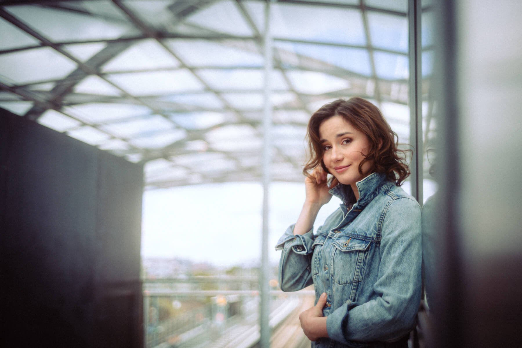 Jeannine Michèle Wacker mit braunen, lockigen Haaren in Jeansjacke posiert am Bahnhof.