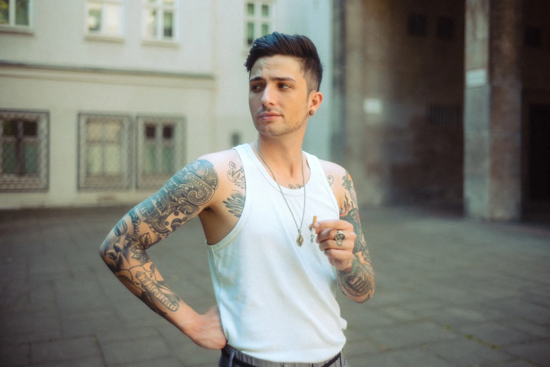 Benjamin Mittelstädt von Berlin Tag und Nacht mit Tattoos trägt weiße Weste, hält Zigarett und steht auf der Straße in der Stadt.