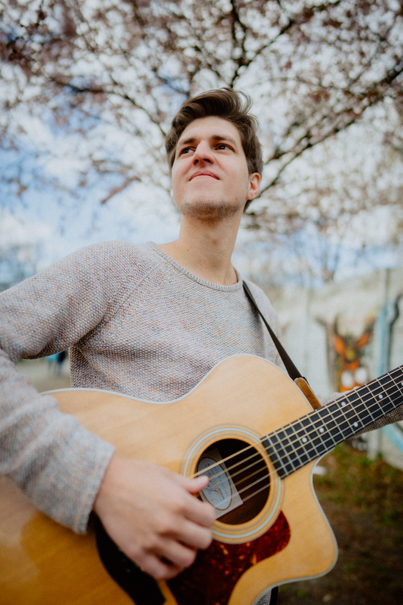 Falk Plücker spielt Gitarre im Freien vor blühenden Bäumen.