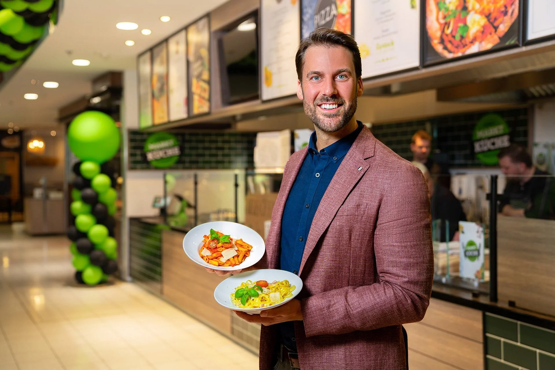 Stephan Cunäus in einem Anzug hält zwei Teller mit Pasta in einem Restaurant.
