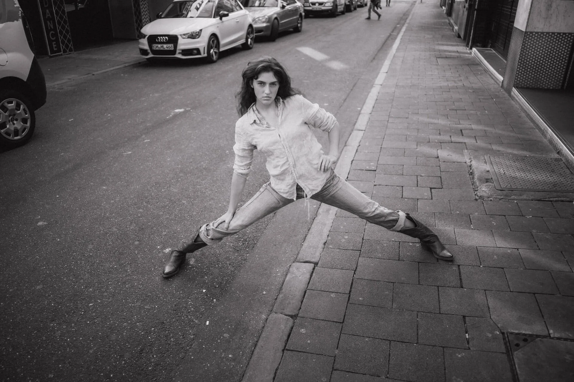 Carlotta Josefine Pahl in Jeans und Hemd steht breitbeinig auf der Straße, blickt ernst in die Kamera, während sie auf der Bürgersteigkante balanciert.