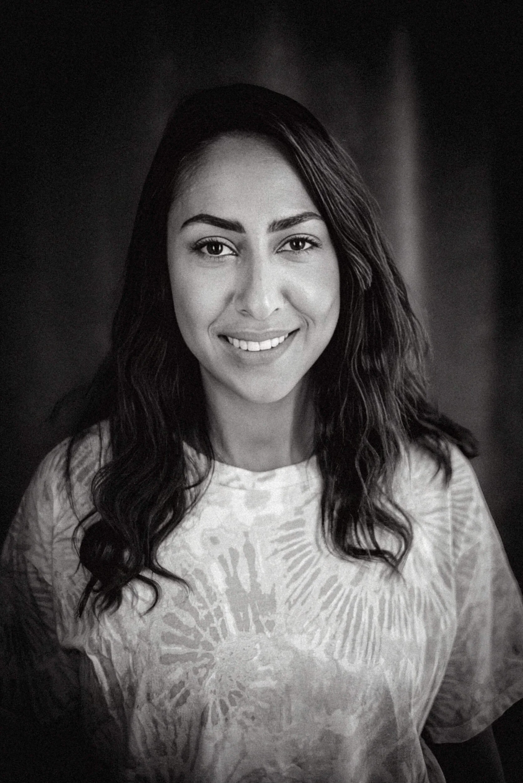 Schwarz-weiß Porträt von Moderatorin Melissa Khalaj mit langen, lockigen Haaren, trägt ein T-Shirt mit Muster.